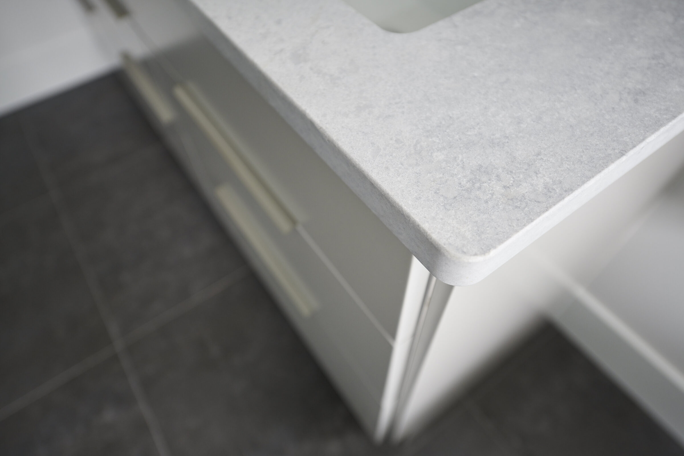 This image shows a close-up of a white kitchen countertop with a minimalist design, set against a background of dark tiled flooring.