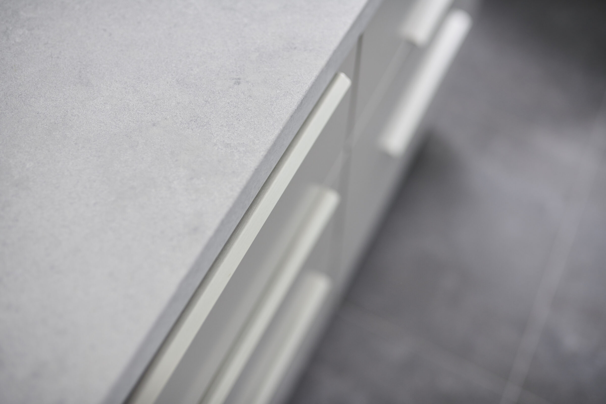 Close-up of a gray countertop with a focus on a cabinet drawer handle, featuring a modern design and minimalist style, against a blurred background.