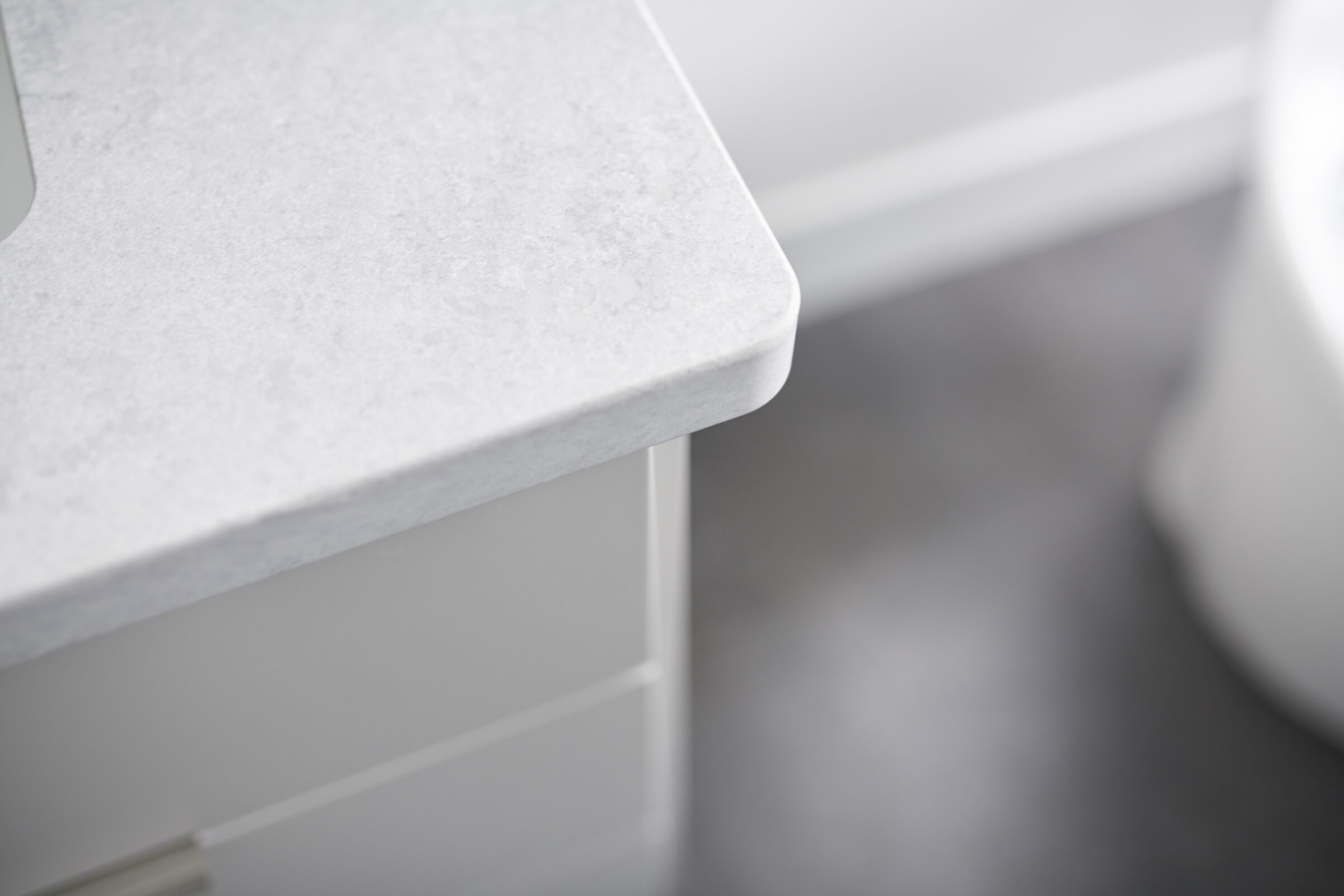 This is a close-up image of a minimalist kitchen counter with a smooth, marble-like finish adjacent to glossy, white drawers with a sleek design.