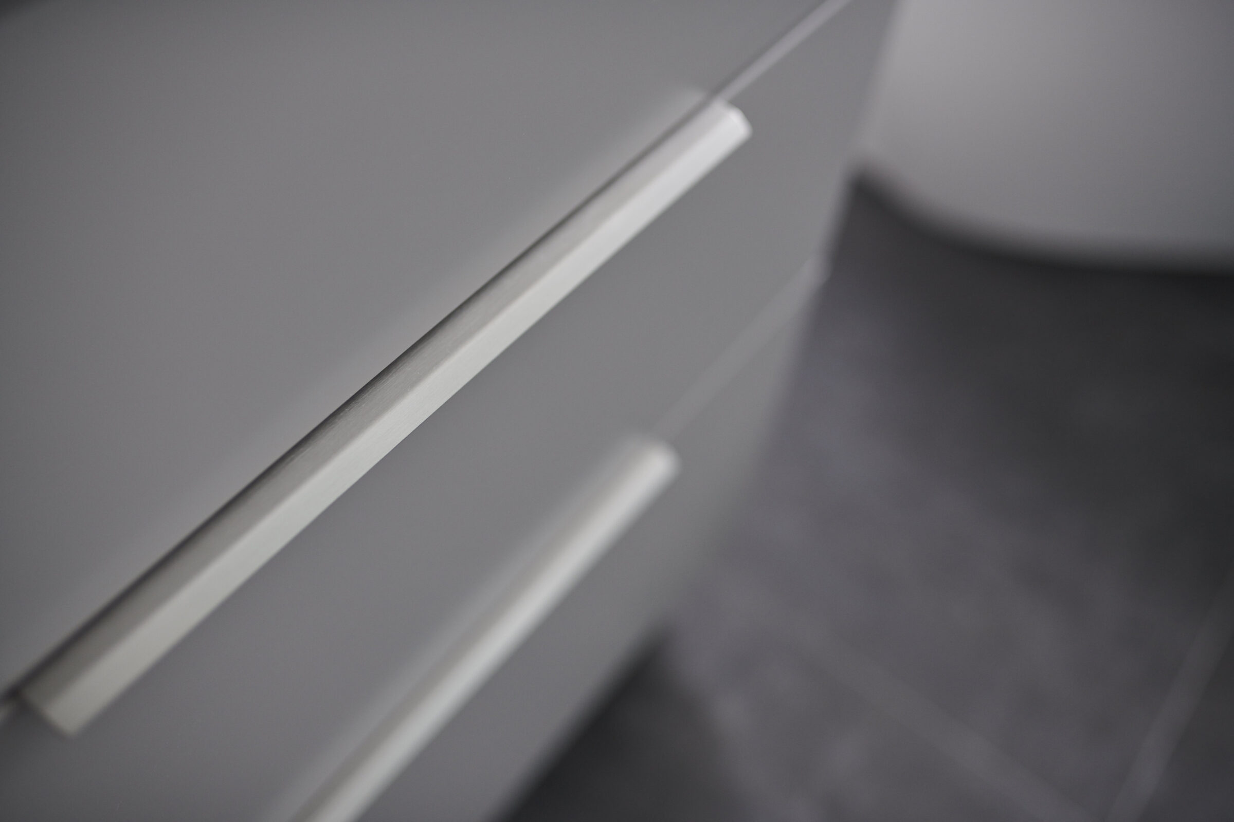 A close-up image of a modern, grey kitchen cabinet with minimalist metallic handles, exhibiting a selective focus and a shallow depth of field.