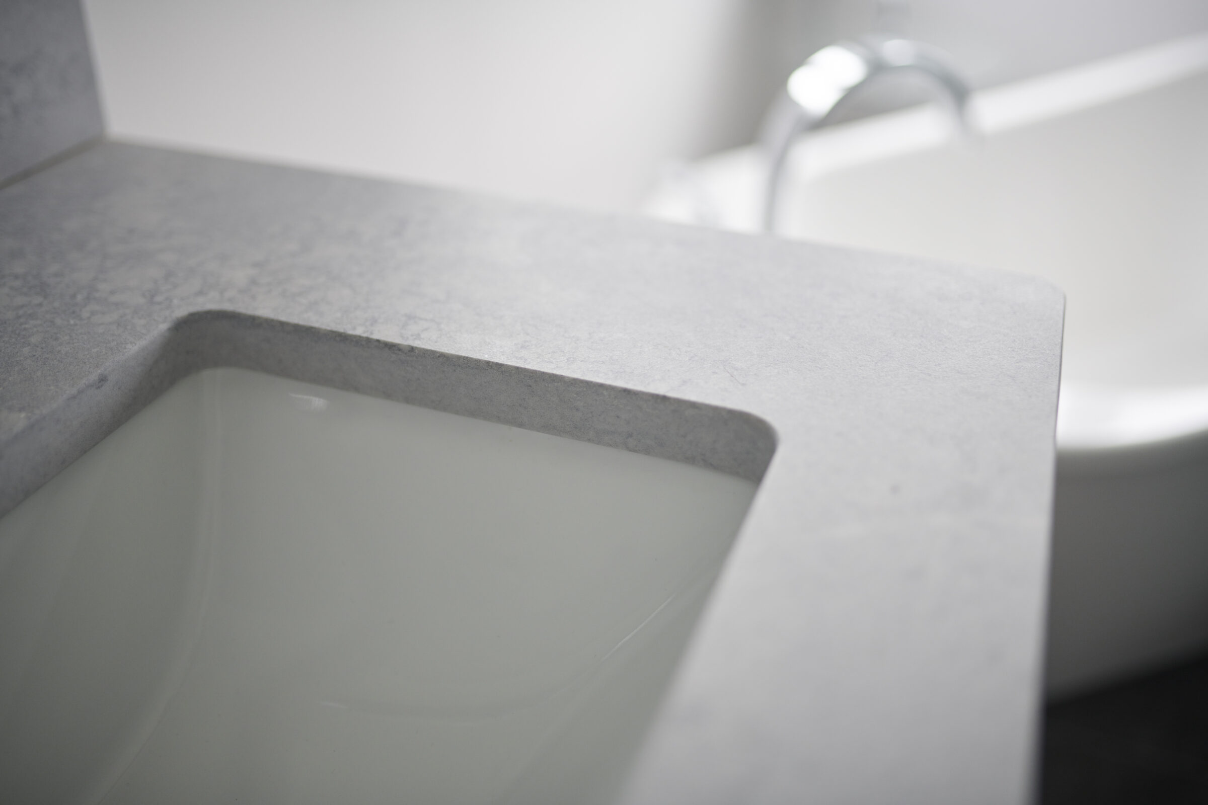 This image shows a close-up view of a modern bathroom, focusing on a gray countertop with an integrated white sink and a blurred toilet in the background.