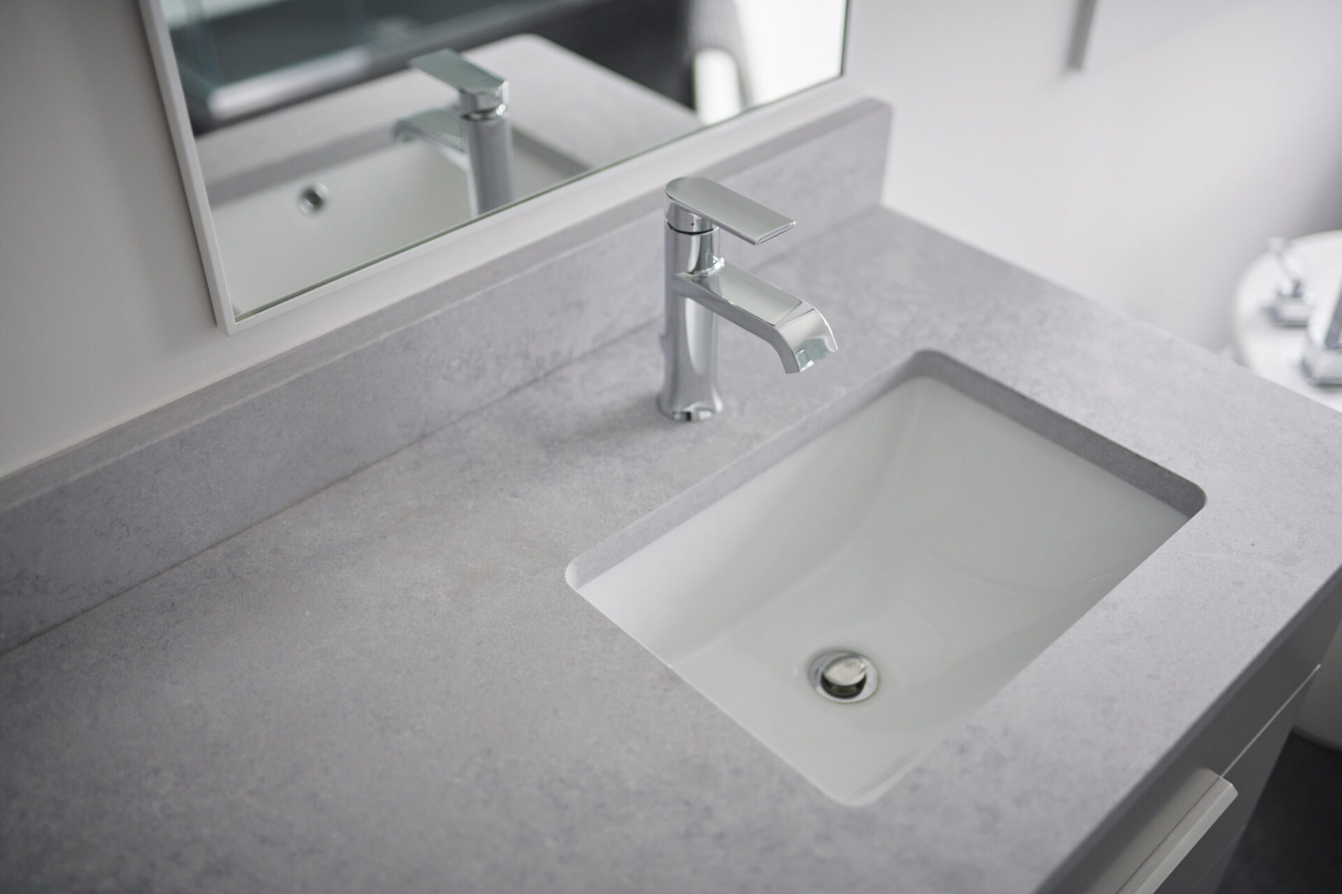 A modern bathroom sink with a chrome faucet set on a gray countertop, with a mirror reflecting the basin above.