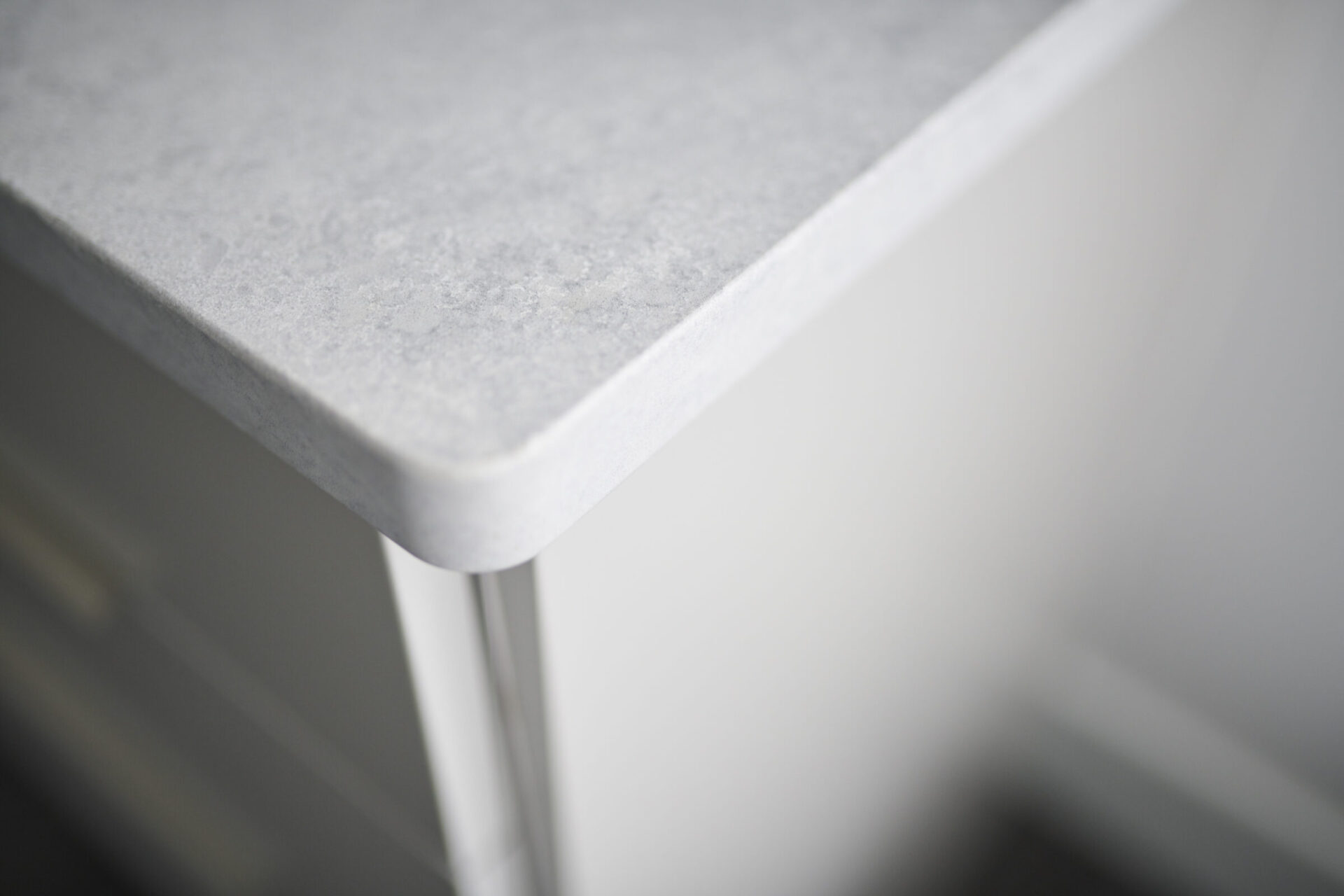 This image shows a close-up of a countertop corner with a subtle rounded edge, featuring a textured surface in soft lighting with a diffuse background.