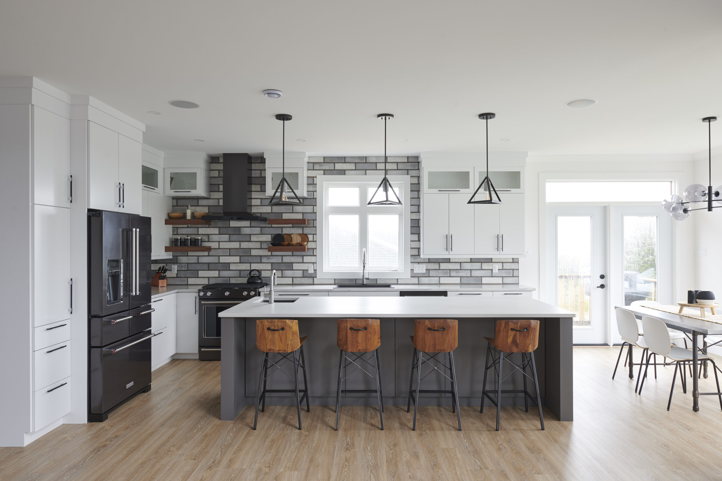 Modern kitchen with white cabinets, gray backsplash, black appliances, pendant lights, a central island with wooden stools, and hardwood floors.