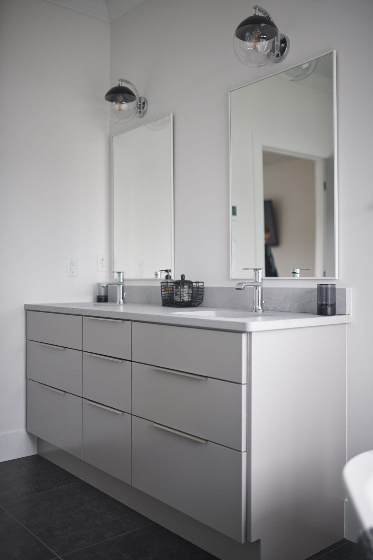 This image shows a modern bathroom vanity with a large mirror, sleek drawers, and minimalistic decor under bright, clear glass sphere wall lights.