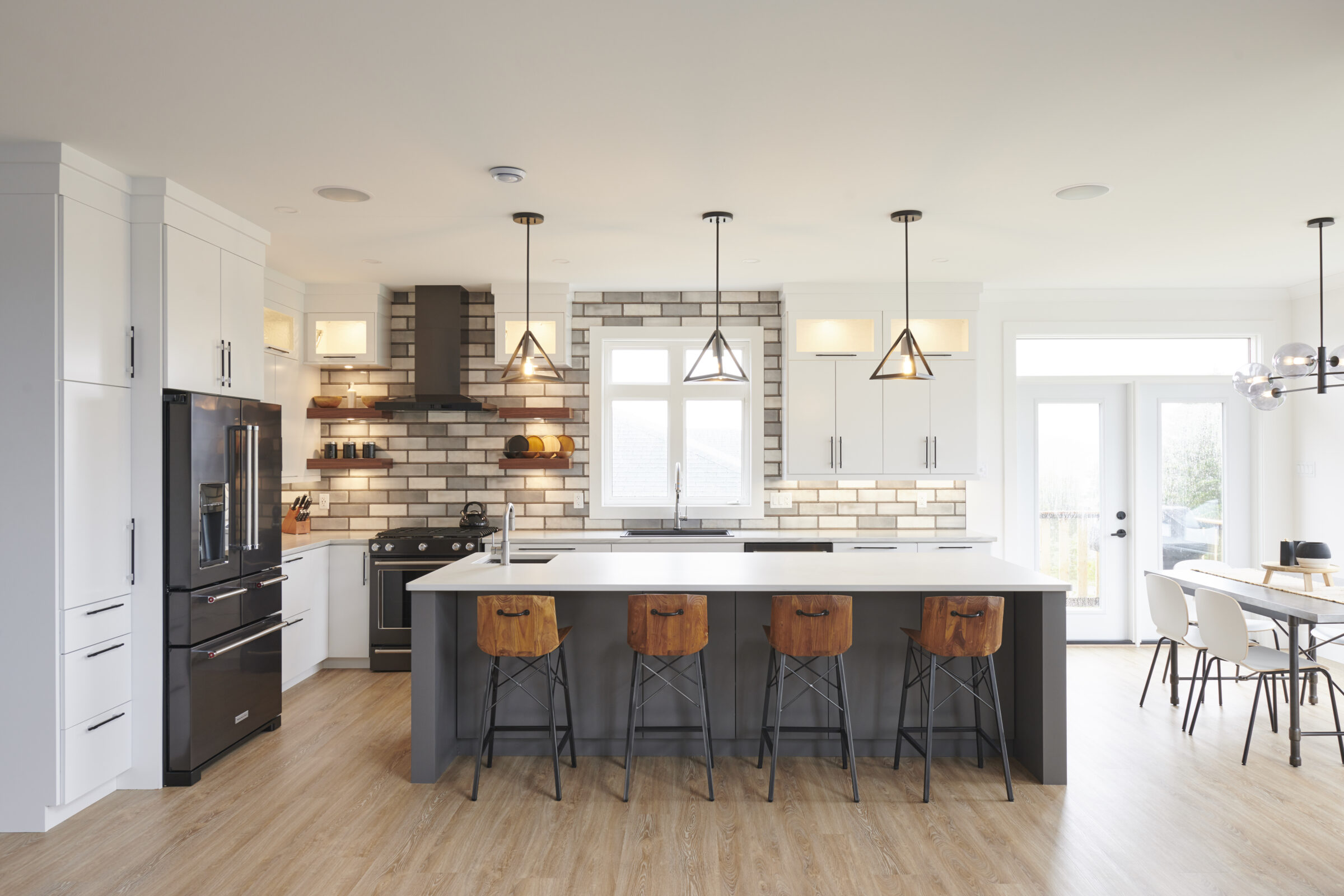 This is a spacious, modern kitchen with white cabinets, stainless steel appliances, pendant lights, a central island, and a wooden floor.