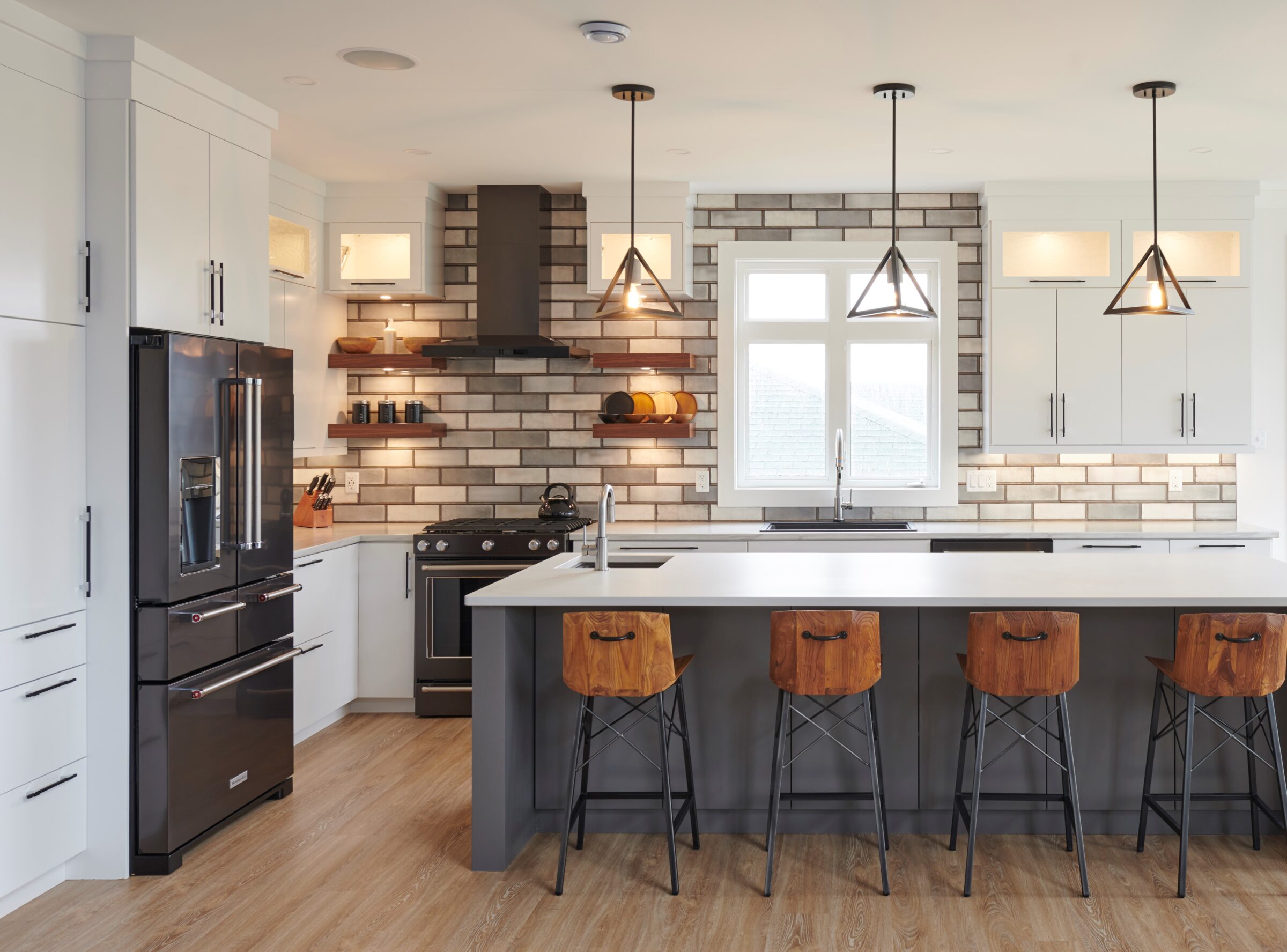 This image shows a modern kitchen with white cabinets, stainless steel appliances, wooden bar stools, and pendant lights over an island.