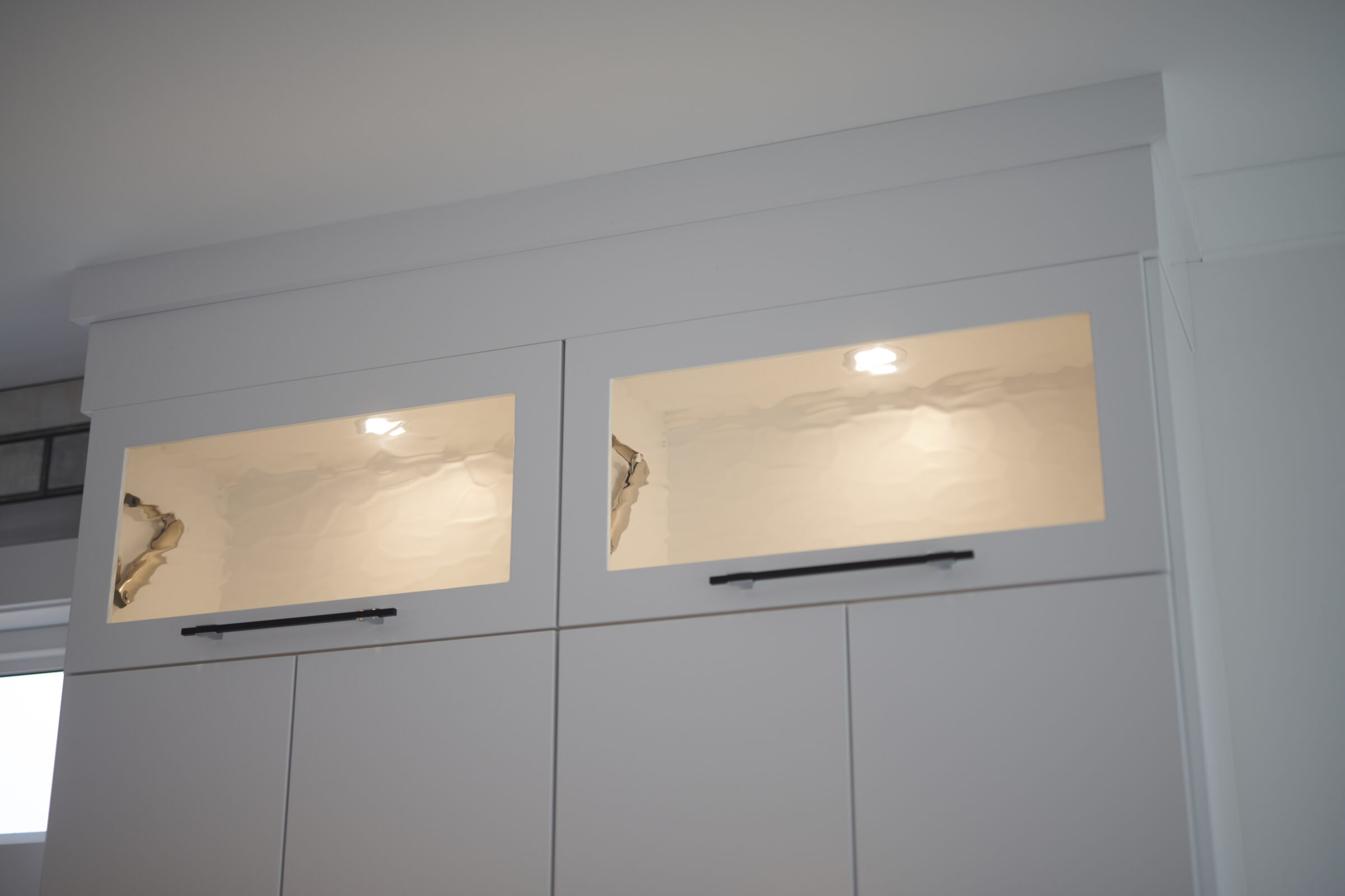 A modern kitchen with white cabinetry featuring two doors with reflective, frosted glass panels, one of which is damaged with a visible crack.