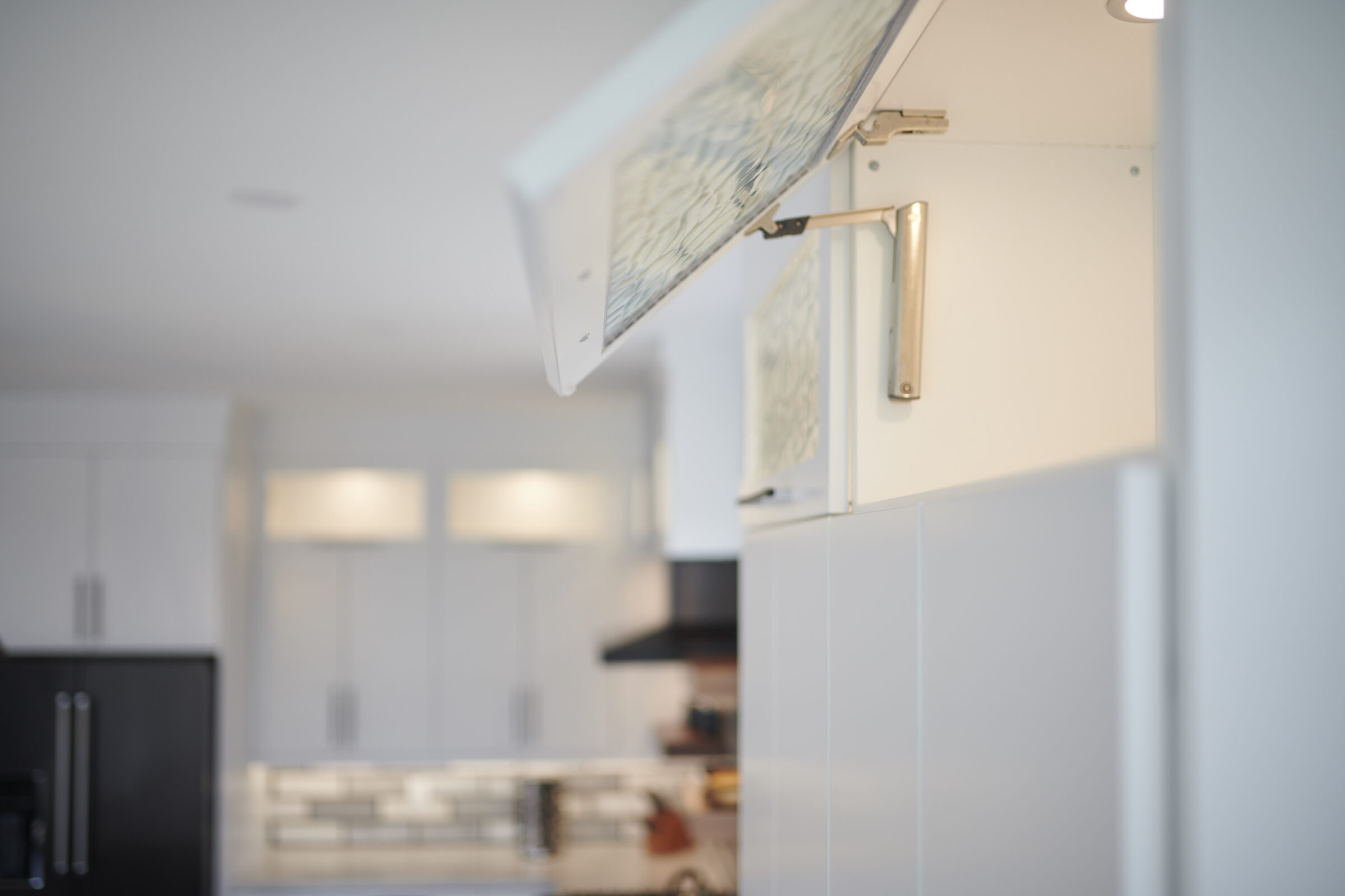 This photo showcases a modern kitchen with white cabinetry, focusing on an open overhead cabinet with a blurred background emphasizing clean design.
