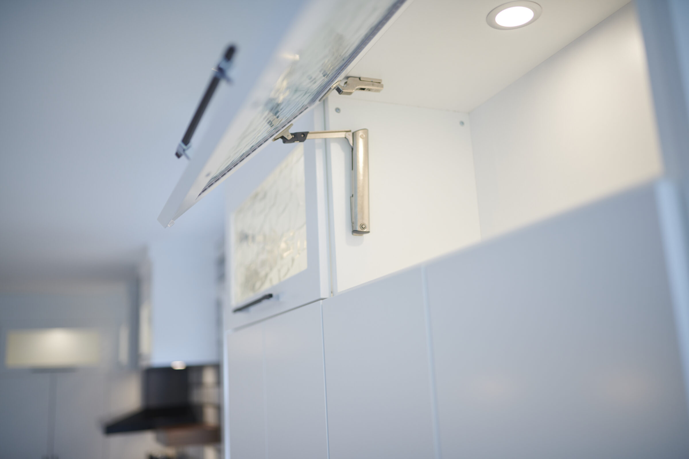Modern kitchen with white cabinets and a lifted cabinet door revealing an organized interior. Stainless steel handle and ambient lighting visible.