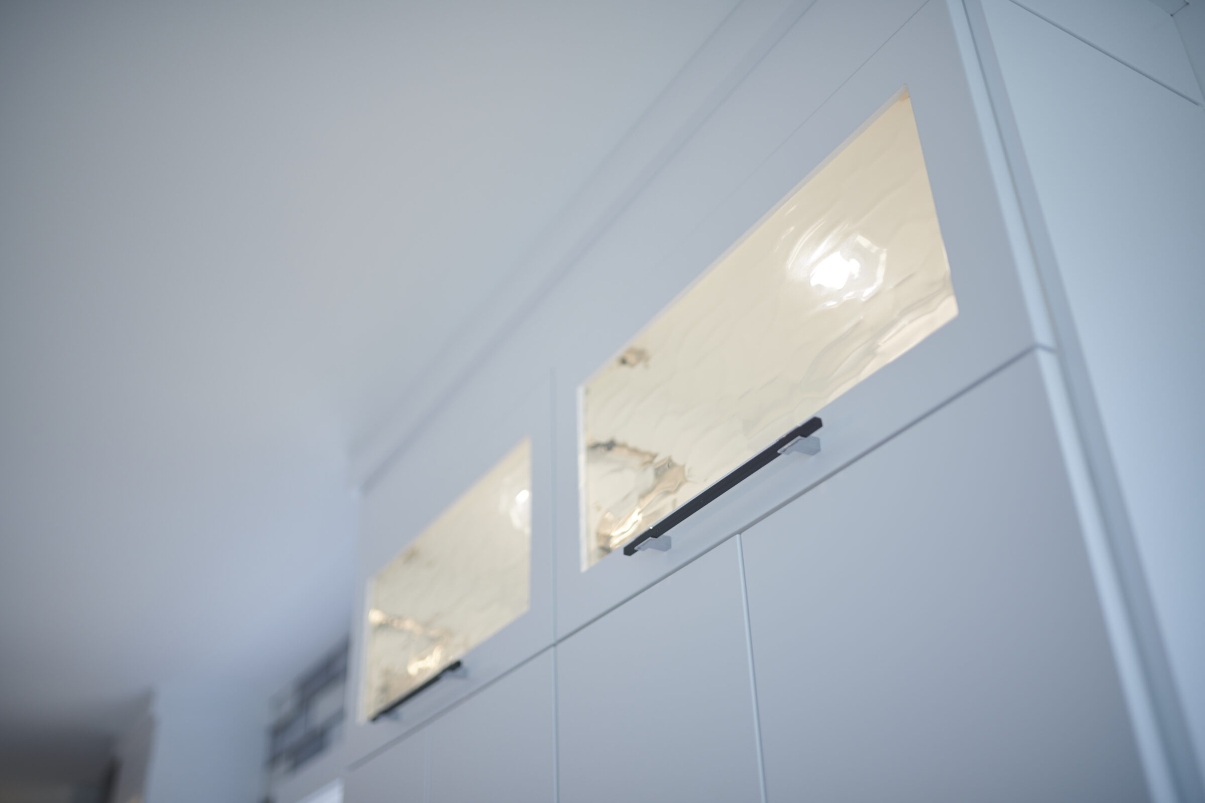 This image shows a modern, white kitchen cabinet with glossy finishes and sleek handles, captured in soft, natural lighting from a high angle.