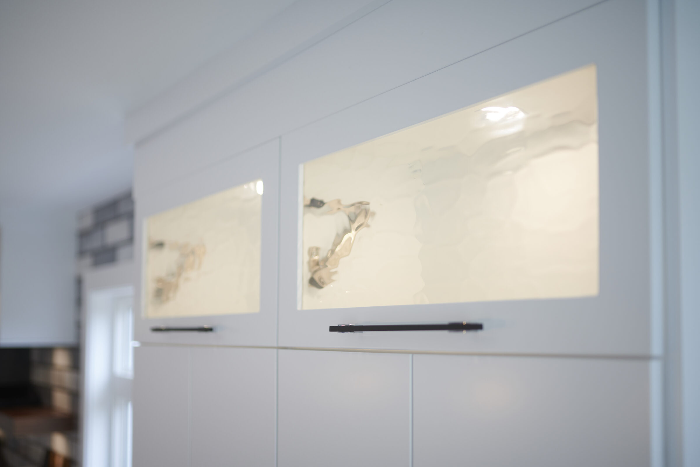 The image shows a modern kitchen with white cabinetry and two abstract artwork pieces mounted on the cupboard doors, creating a minimalist aesthetic.