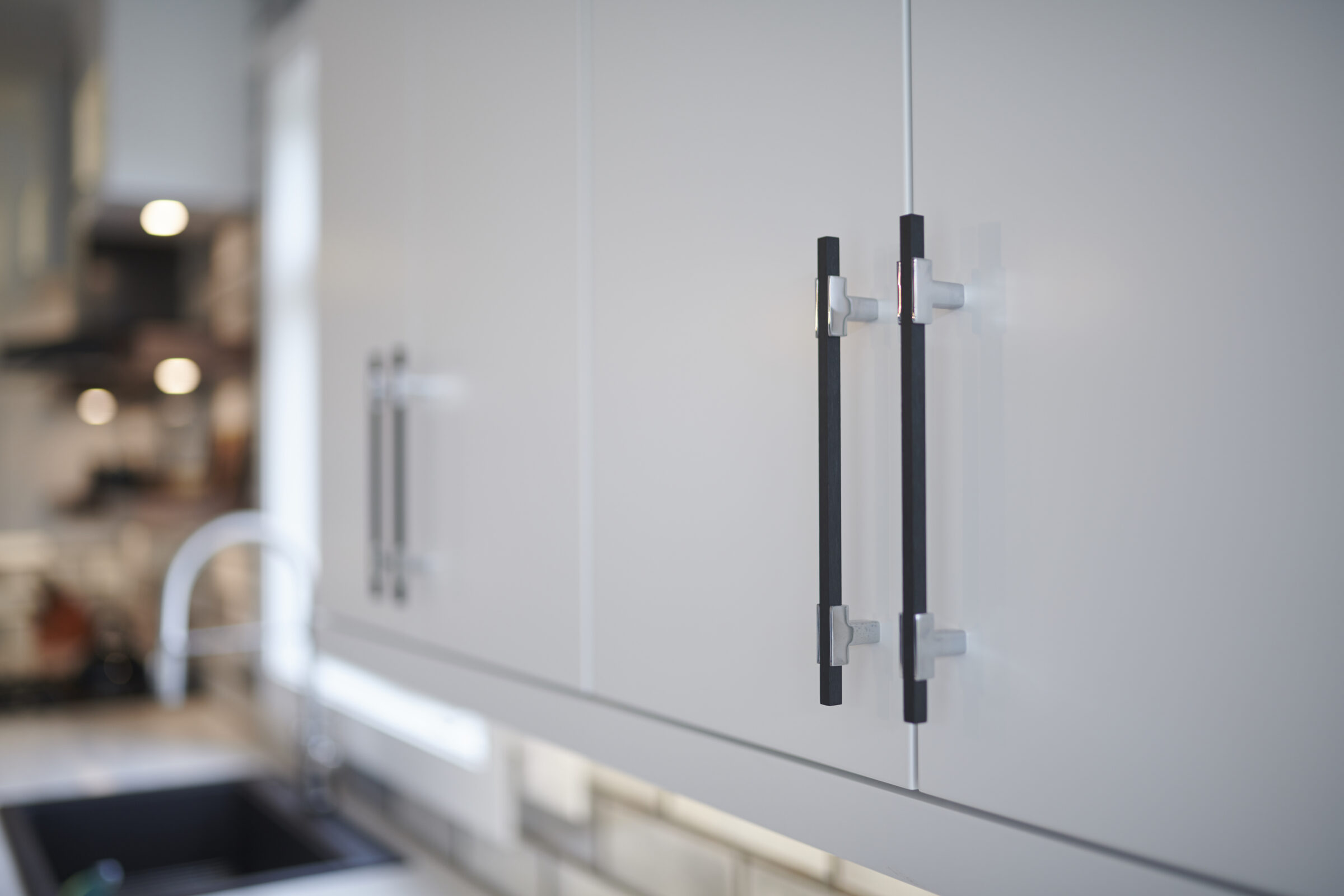 Close-up of modern kitchen cabinet with sleek black handles, shallow depth of field, blurred background showcasing a minimalist, contemporary interior design style.