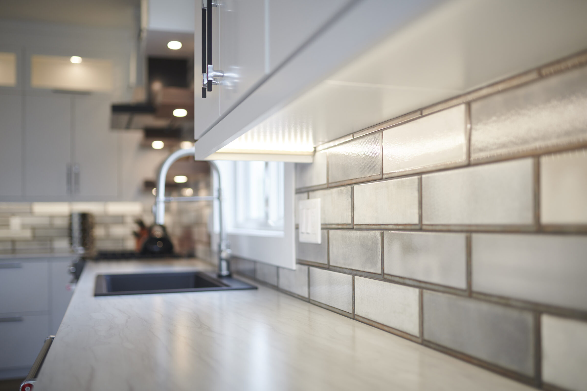 Modern kitchen with white cabinets, subway tile backsplash, marble countertops, stainless steel faucet, and an undermount sink, exhibiting a clean, minimalist design.