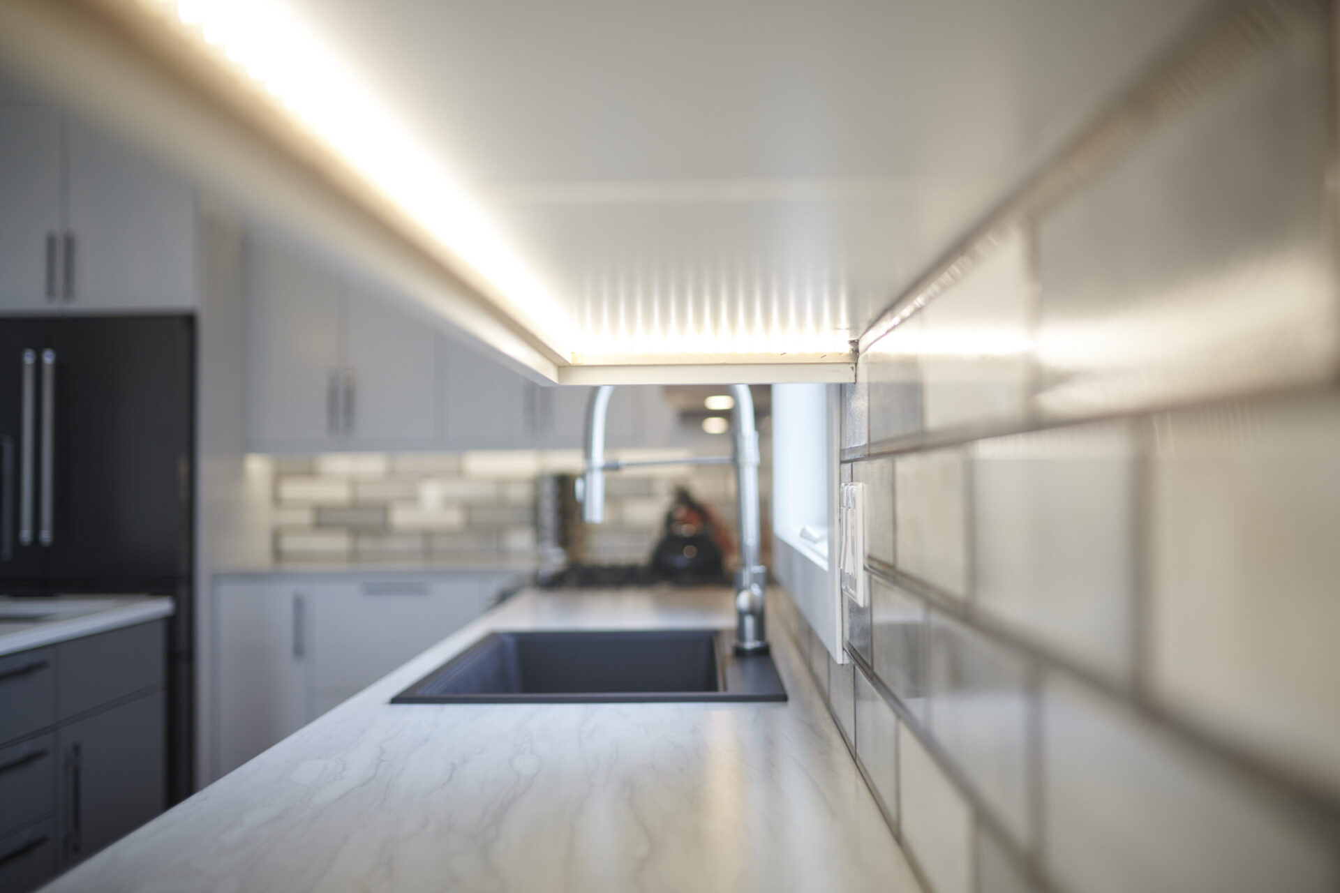 A modern kitchen interior focused on a white marble countertop with an under-cabinet light; blurred background showcasing appliances and cabinetry.