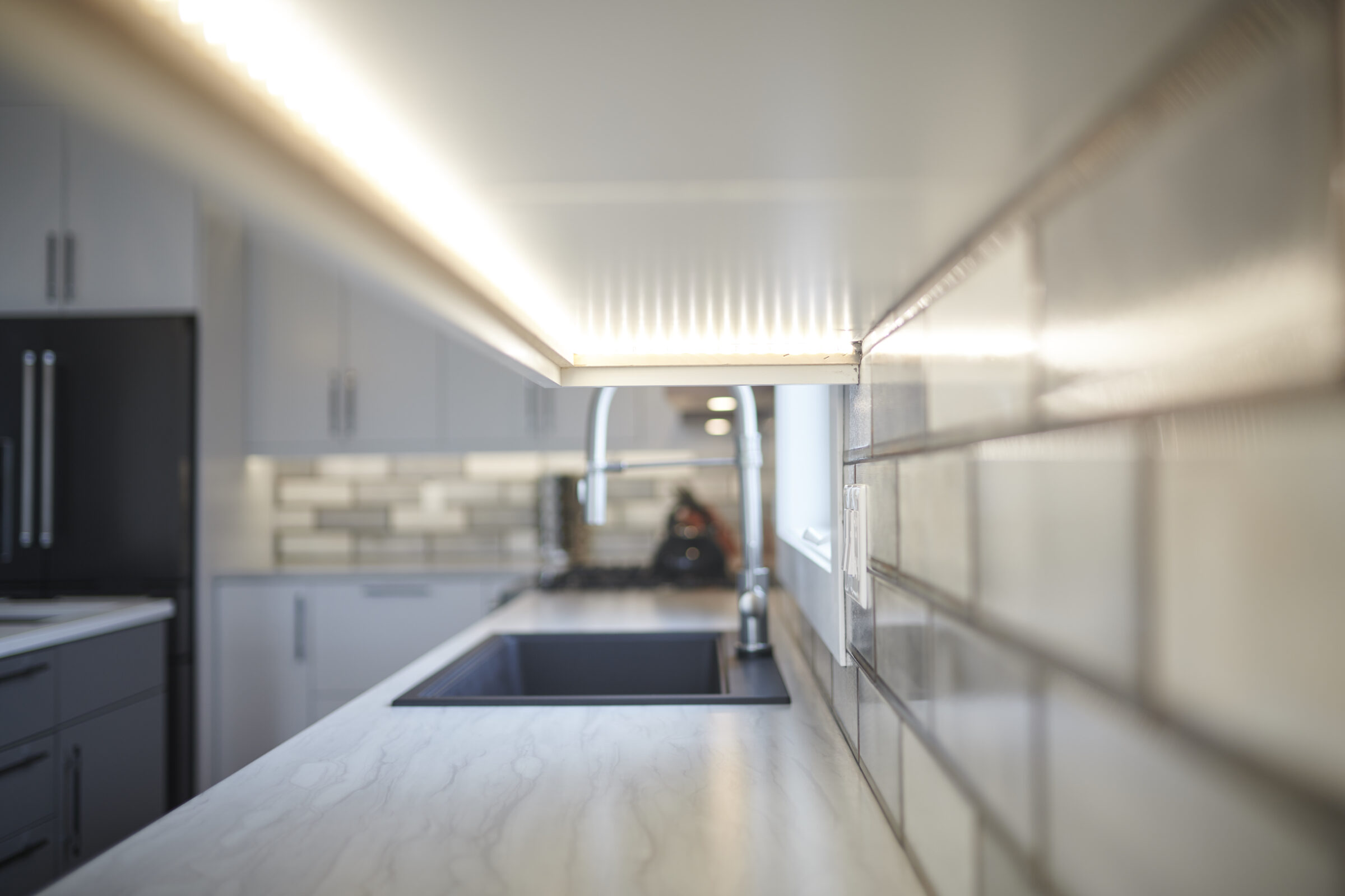 A modern kitchen interior focused on a white marble countertop with an under-cabinet light; blurred background showcasing appliances and cabinetry.