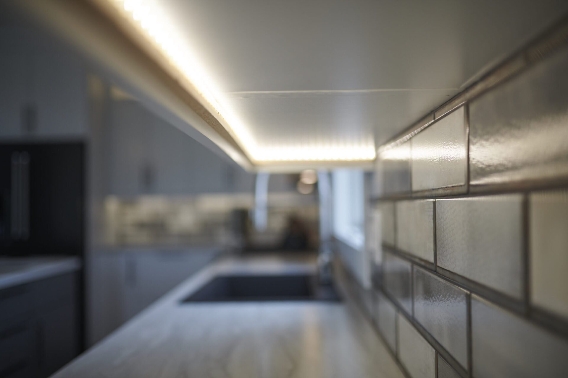 A modern kitchen with LED lighting under cabinets, showcasing a blurred background focused on glossy subway tiles and reflecting a sleek counter.