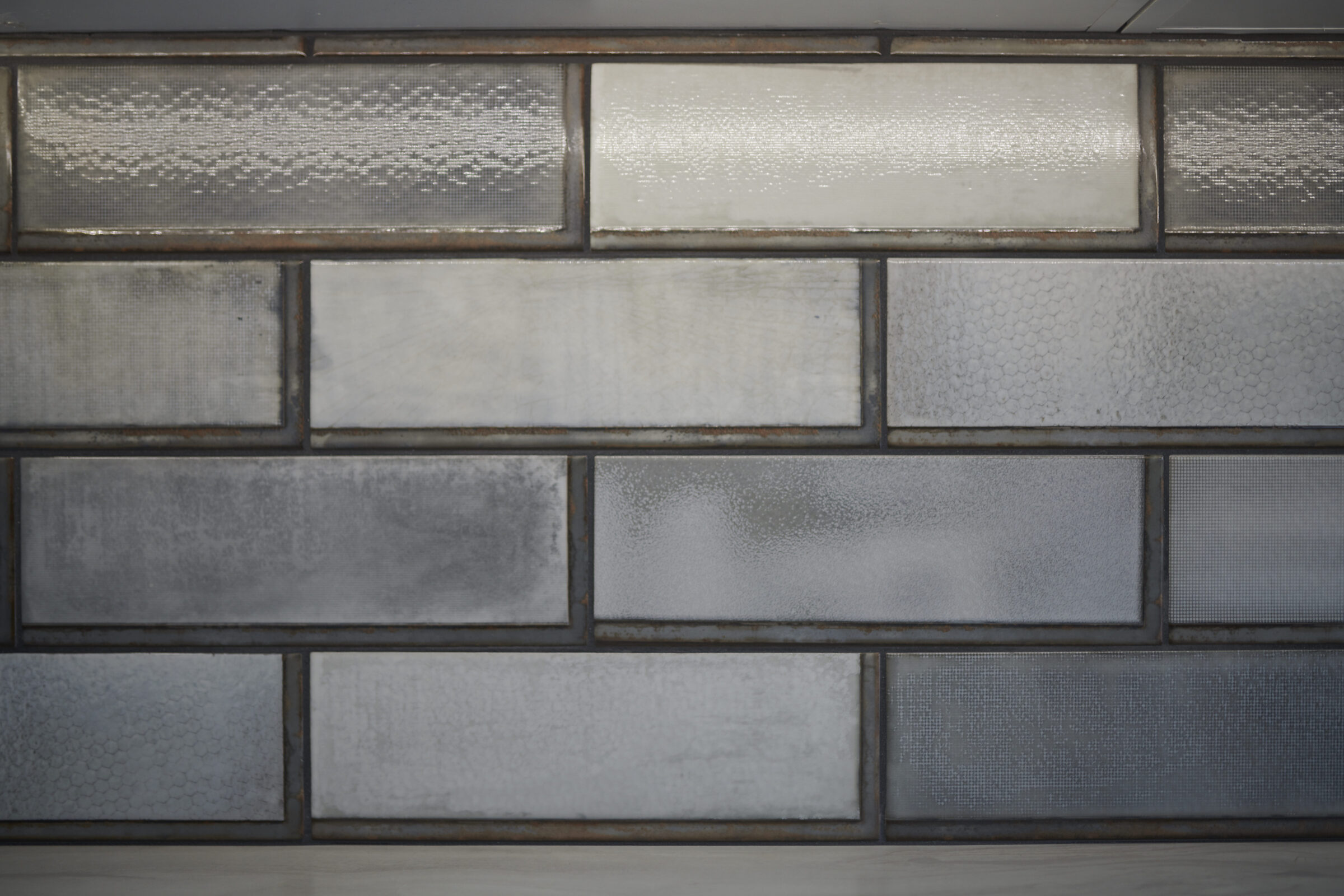 The image shows a textured wall with a variety of rectangular glass blocks creating an abstract pattern in muted gray tones.