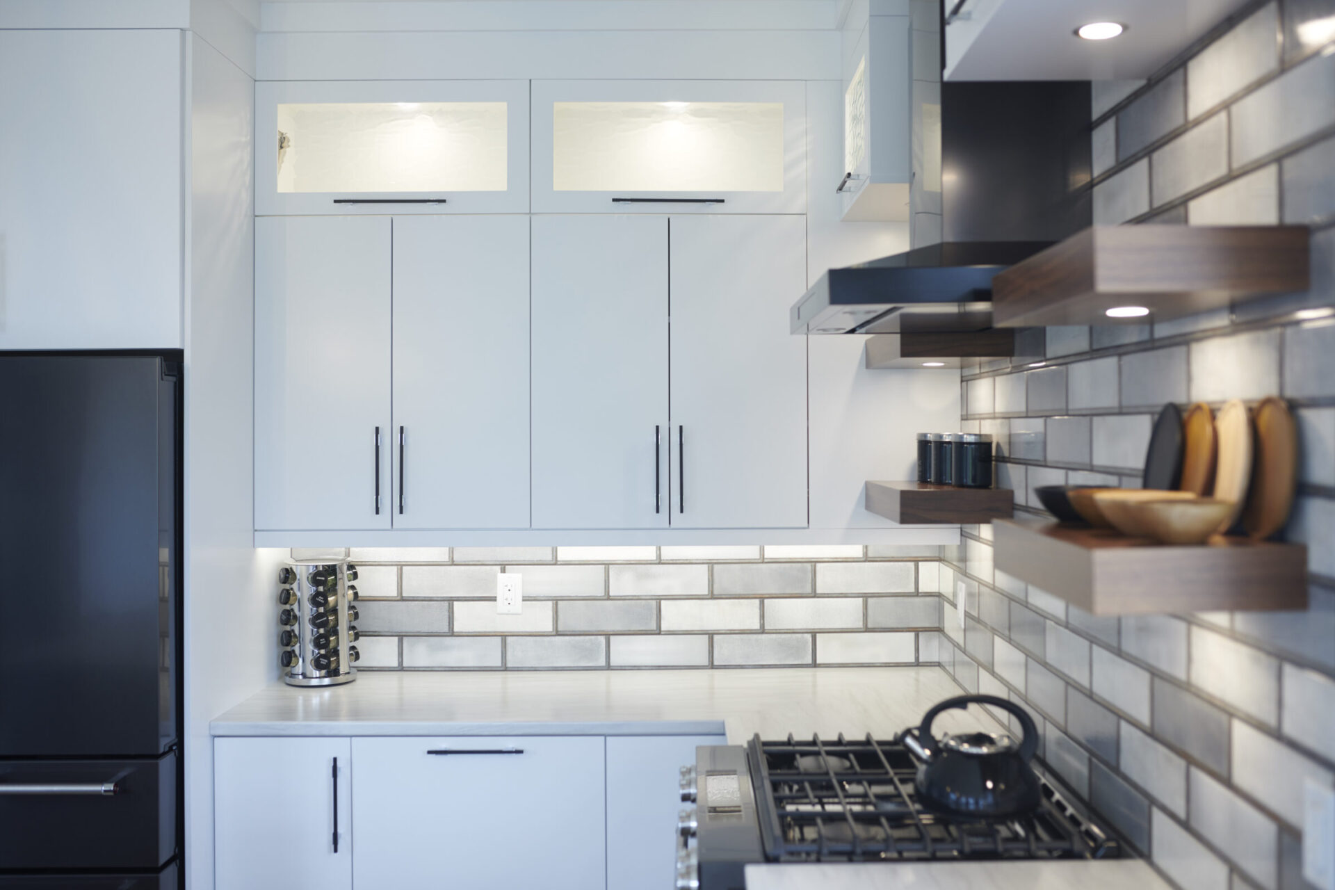 Modern kitchen interior with white cabinets, subway tile backsplash, stainless steel appliances, floating shelves, and dark countertop. Clean, organized, with natural light.