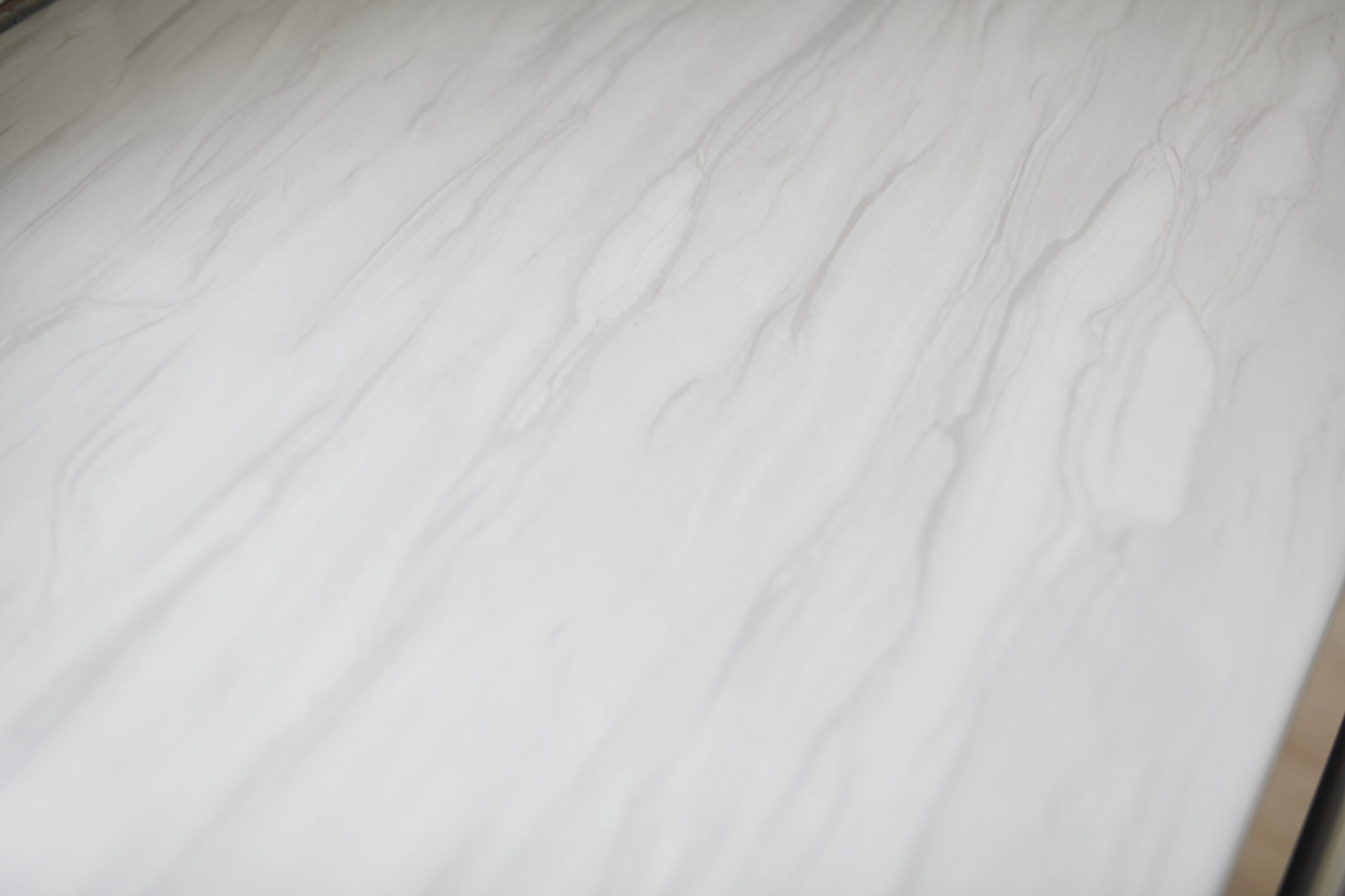 The image shows a smooth, white marble surface with delicate gray veins running throughout. It's bright with a subtle sheen, indicating quality material.