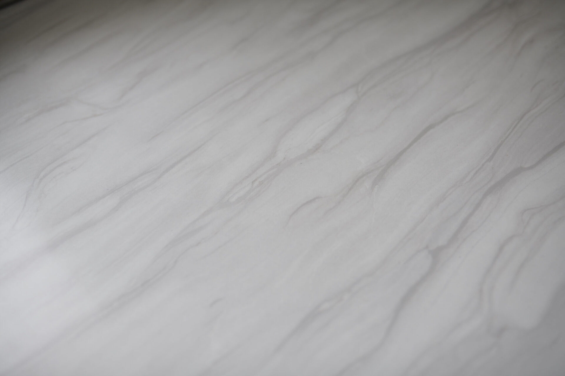 The image shows a close-up of a smooth surface with a marble pattern, predominantly in shades of white and gray, with subtle veining throughout.