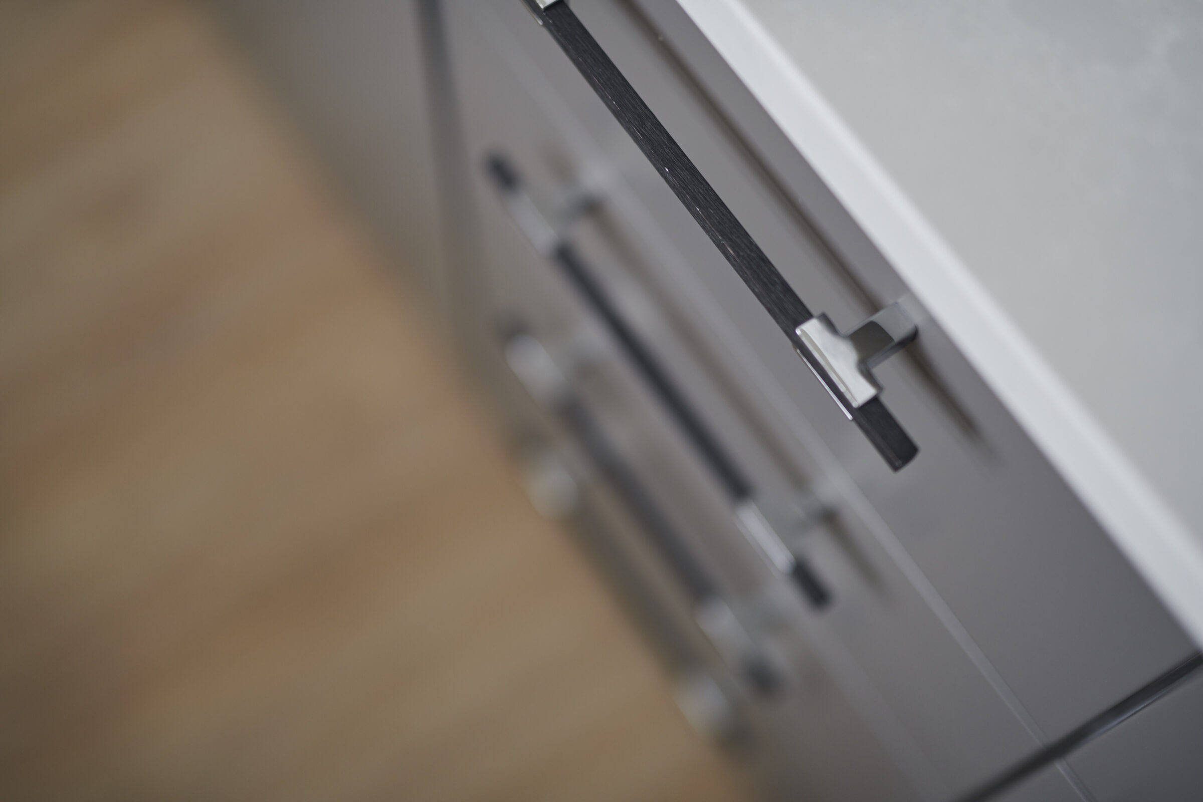 This image features a close-up of a gray storage unit with black handles, showcasing a sleek design with a blurred wooden floor background.