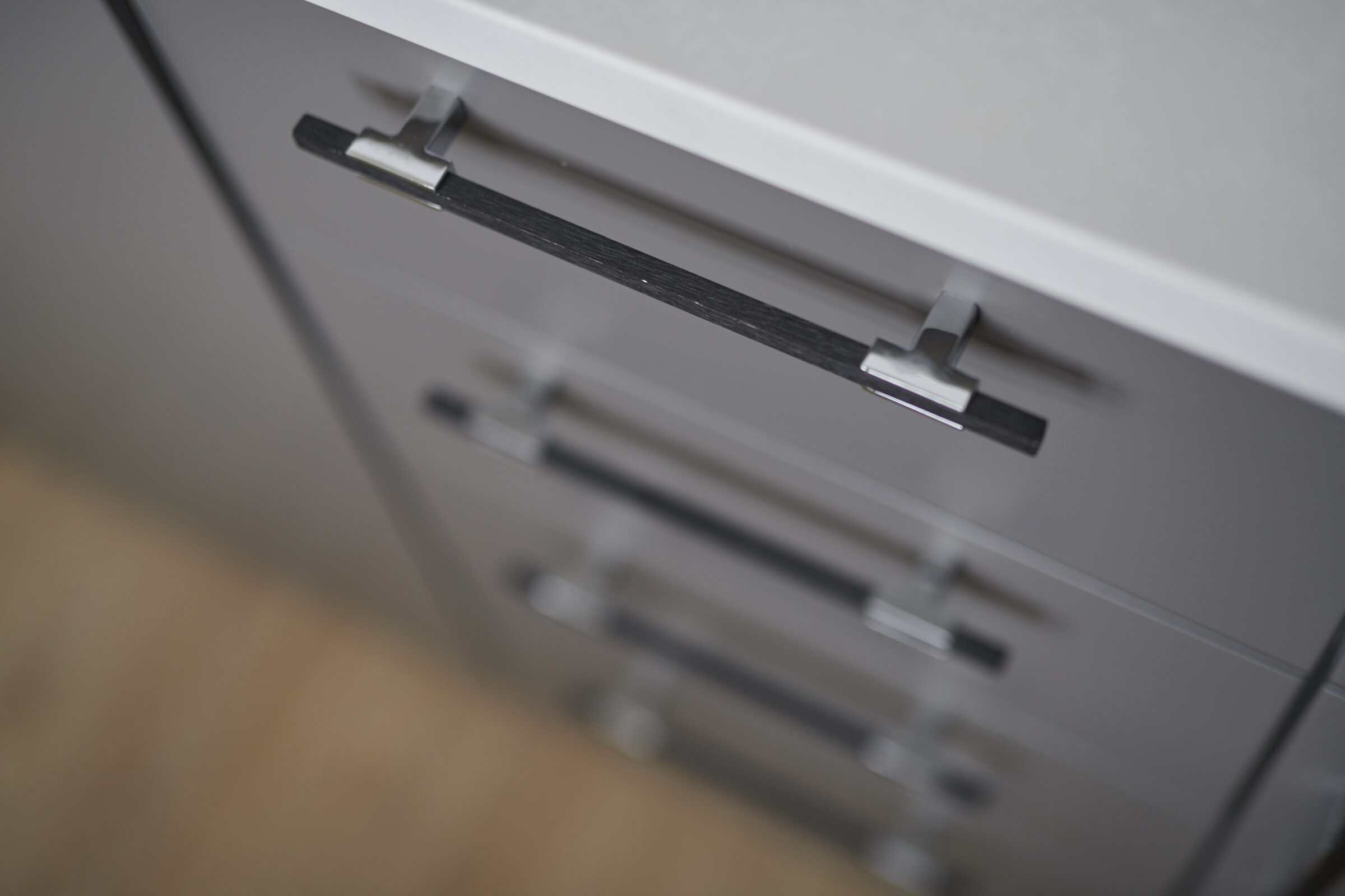 The image shows a close-up of a grey filing cabinet with multiple drawers, each featuring a modern, silver metal handle against a blurred background.