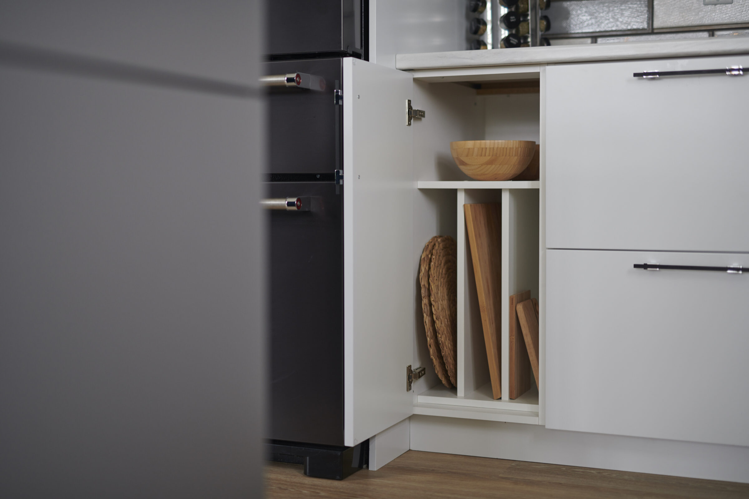 A modern kitchen cabinet is partially open, revealing wooden bowls and cutting boards. There's a wine rack in the background, and the décor is minimalist.
