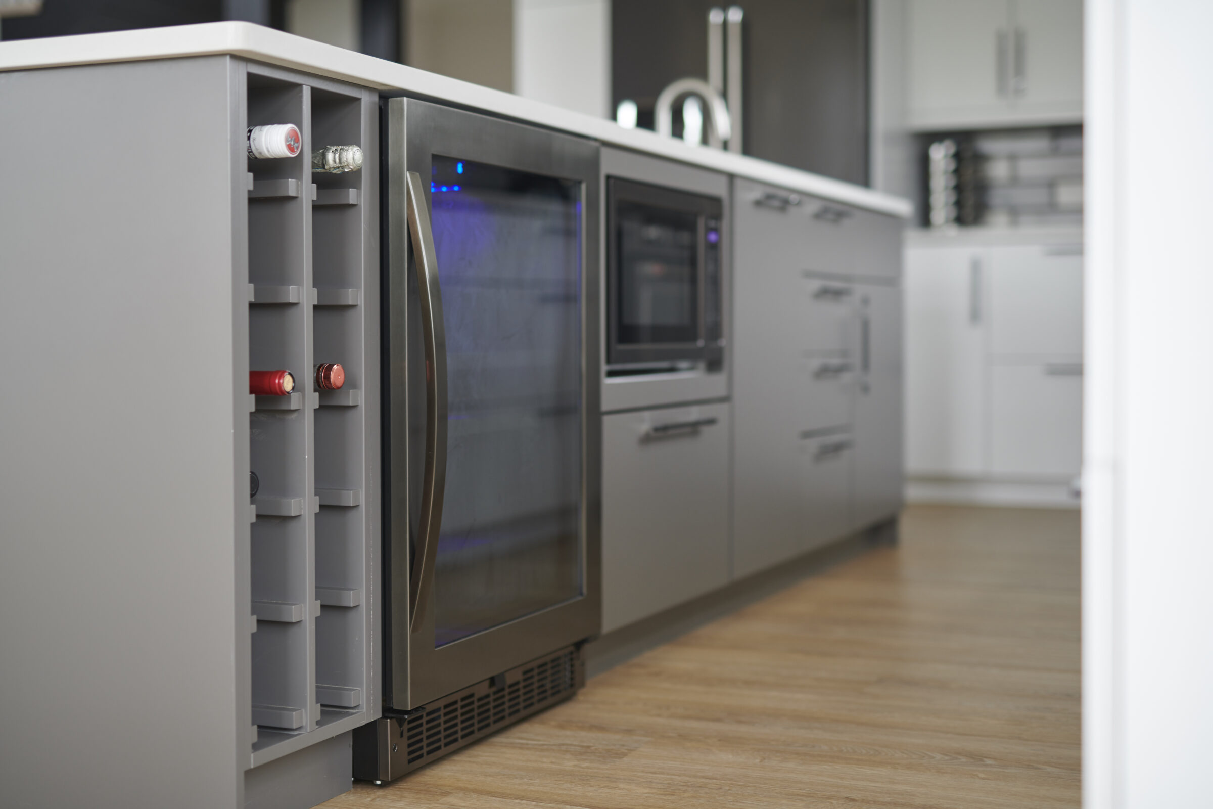 A modern kitchen interior with stainless steel appliances, including a large refrigerator. Wooden flooring complements the gray cabinetry and white counters.