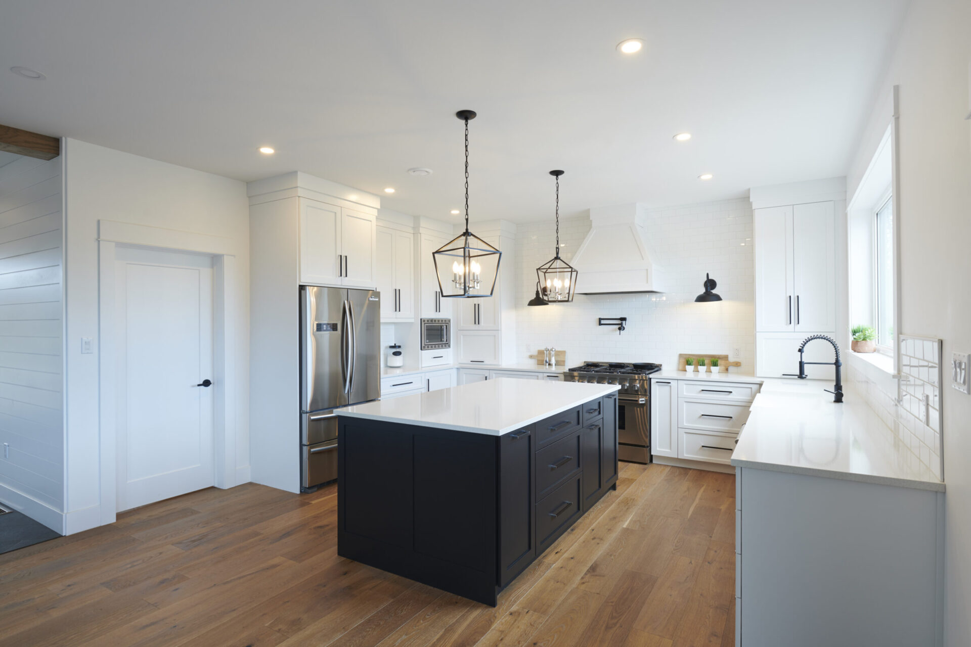 Modern kitchen with white cabinets, dark island, stainless steel appliances, pendant lights, and hardwood floors. Bright, clean, contemporary design.