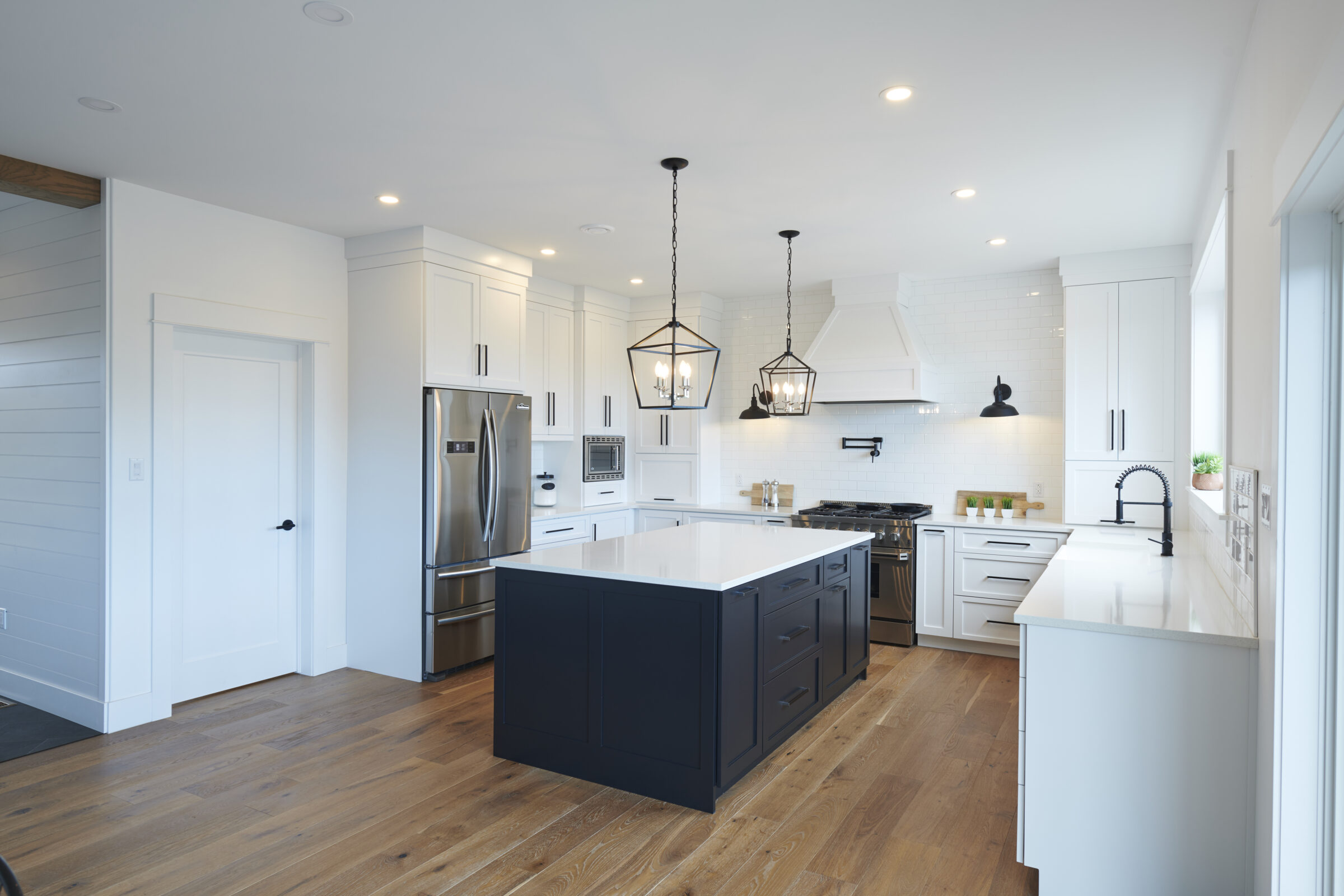 Modern kitchen with white cabinetry, stainless steel appliances, a dark island, pendant lights, hardwood floors, and subway tile backsplash. Bright and clean design.
