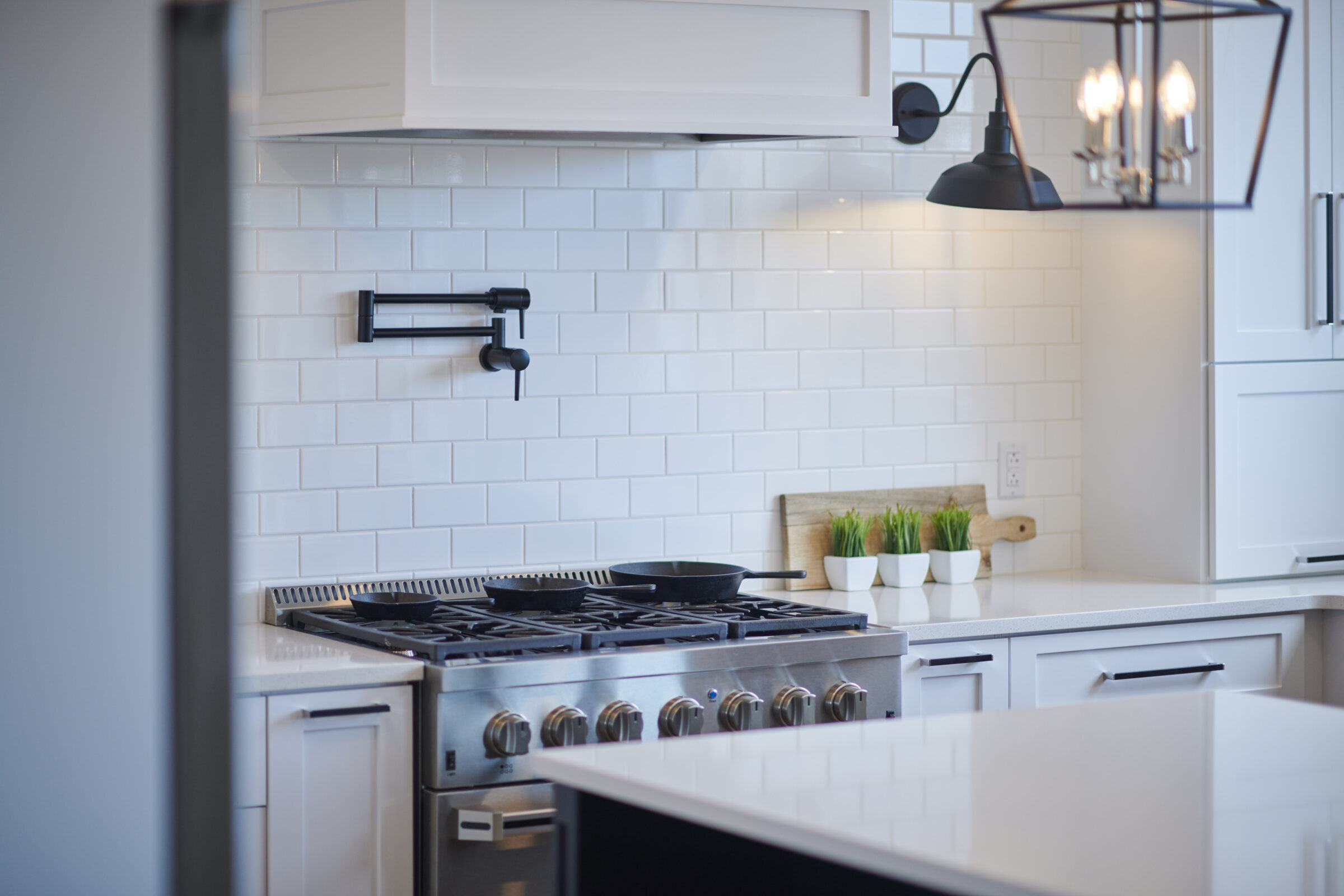 A modern kitchen with white cabinets, subway tile backsplash, stainless steel gas stove, and a black accent wall-mounted pot filler faucet.