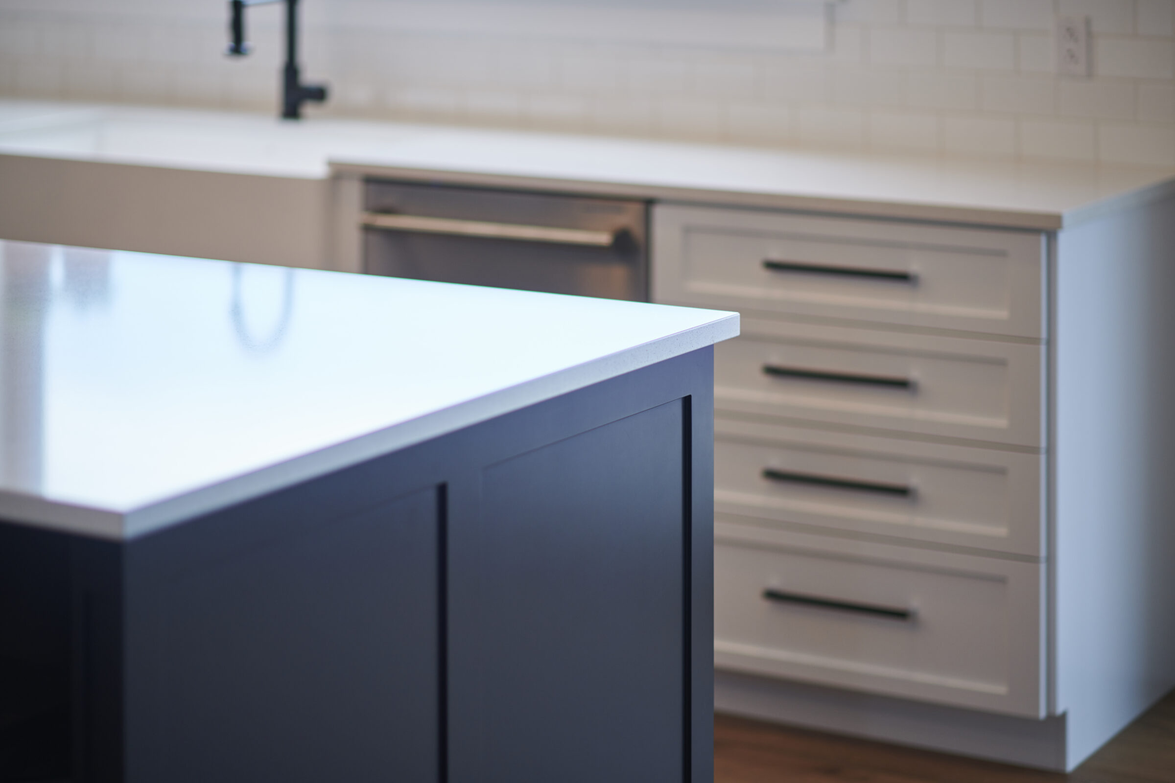 A modern kitchen interior featuring a dark gray island countertop in focus, with white cabinetry and drawers in the background, all under soft lighting.