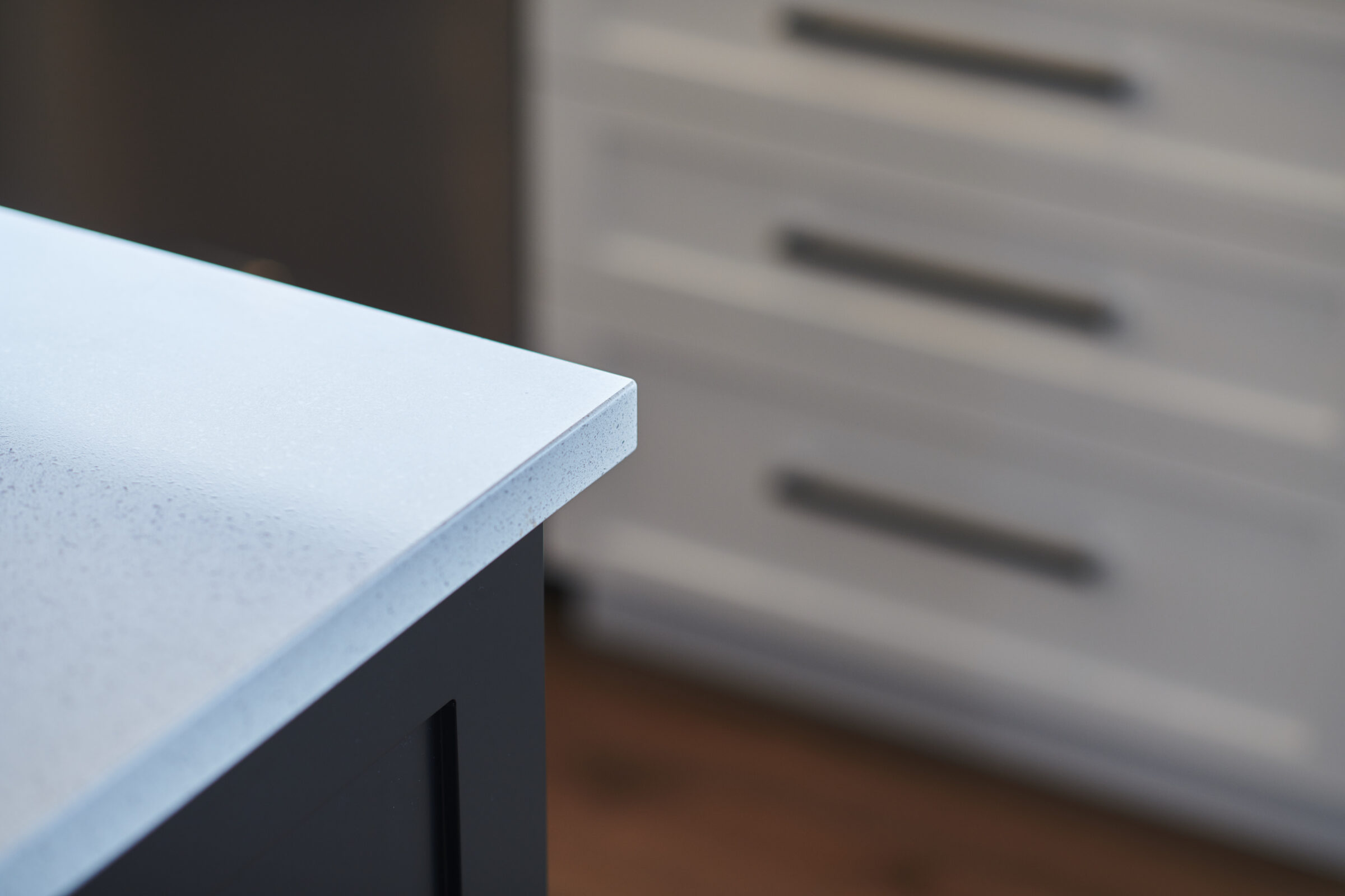 This image shows a close-up of a white speckled countertop edge with a blurred white drawer unit in the background, in a softly lit room.
