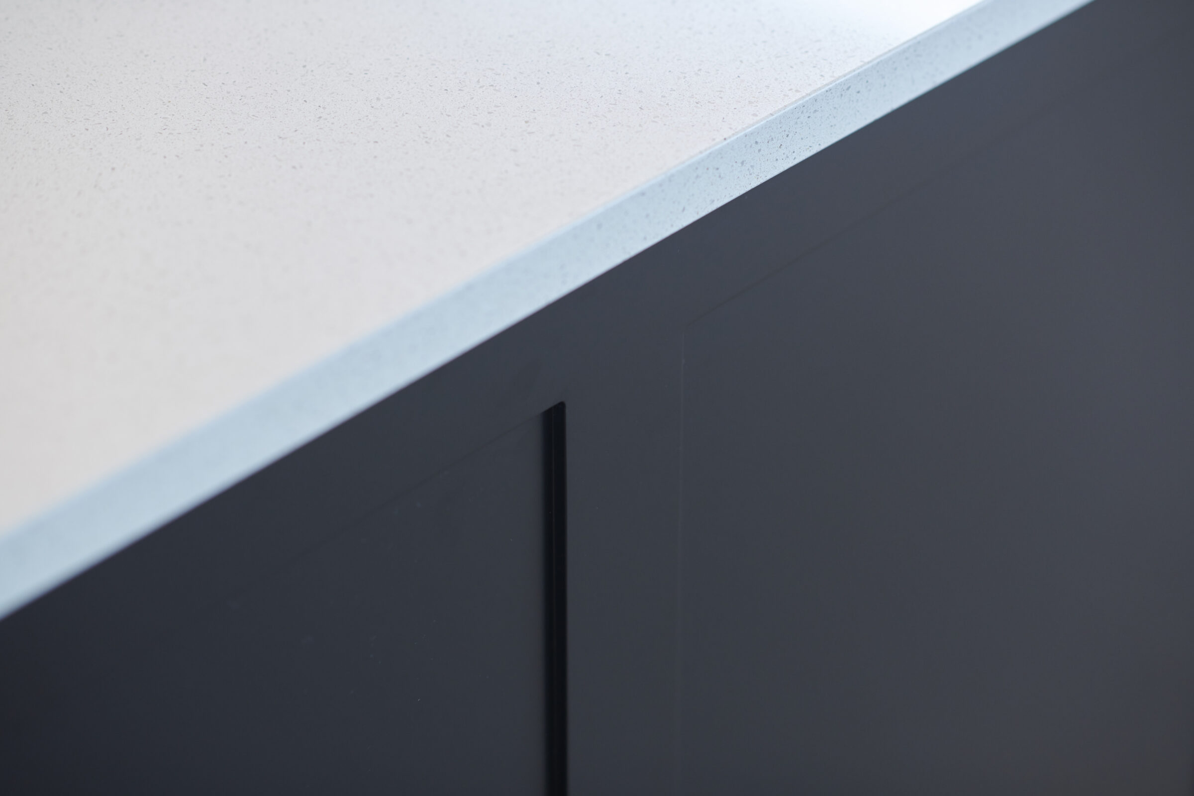The image shows a close-up of a modern kitchen with a speckled countertop and dark cabinetry, focusing on the textures and materials.