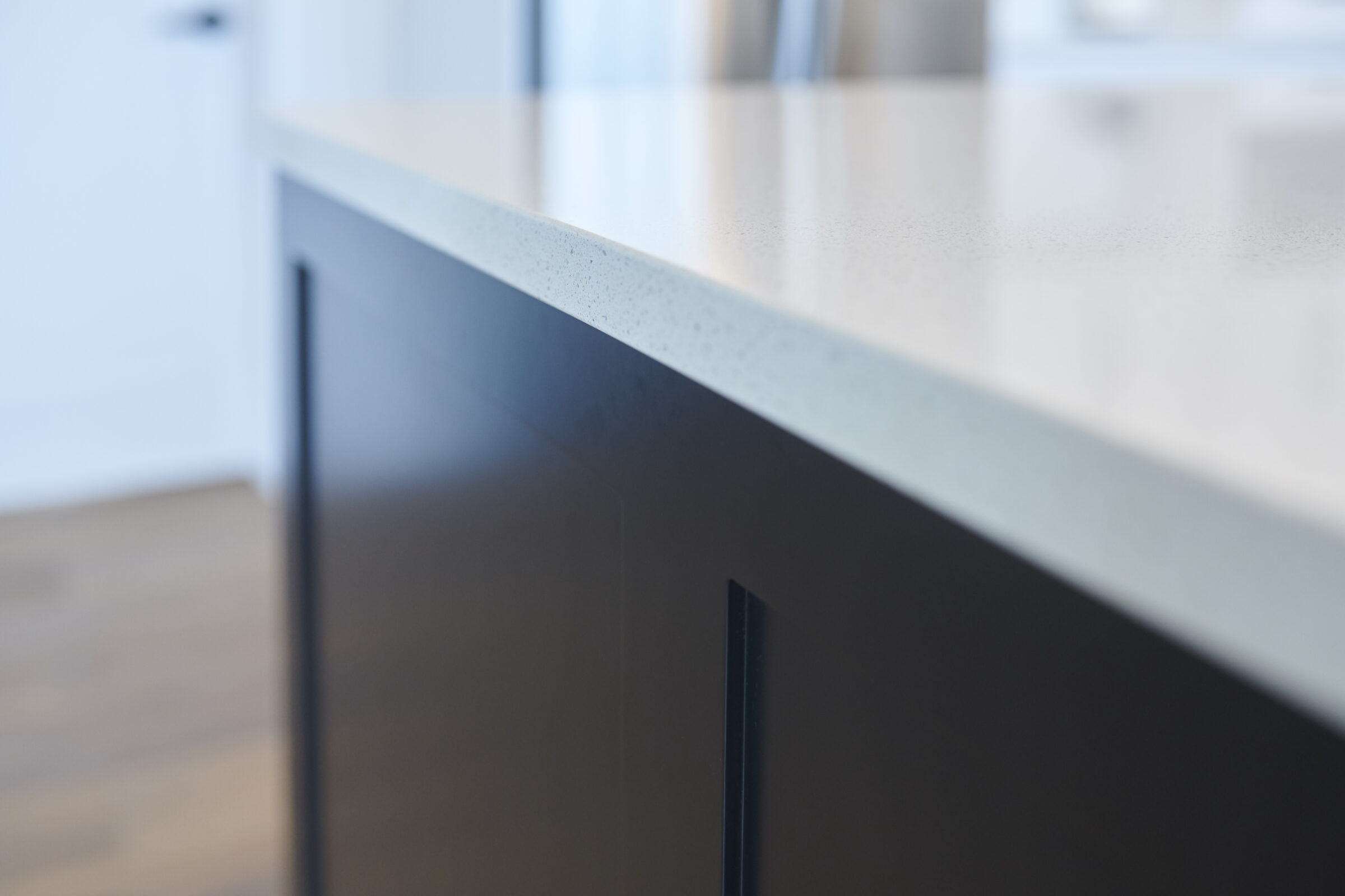 The image shows a close-up side view of a modern kitchen countertop with a matte finish on the cabinet. The background is out of focus.
