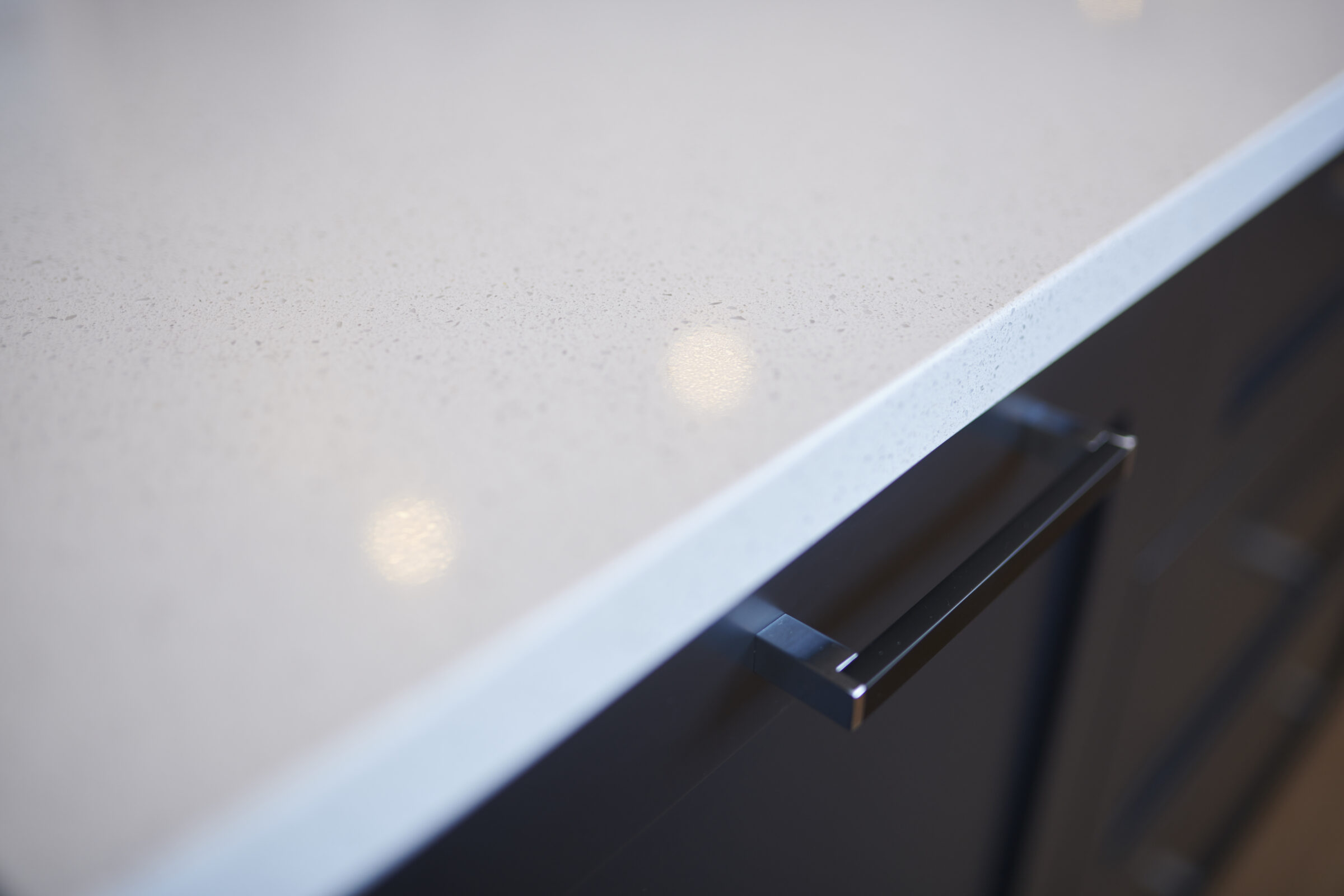 This image shows a close-up of a modern kitchen countertop with a speckled pattern and a sleek, dark cabinet drawer with a contemporary handle.