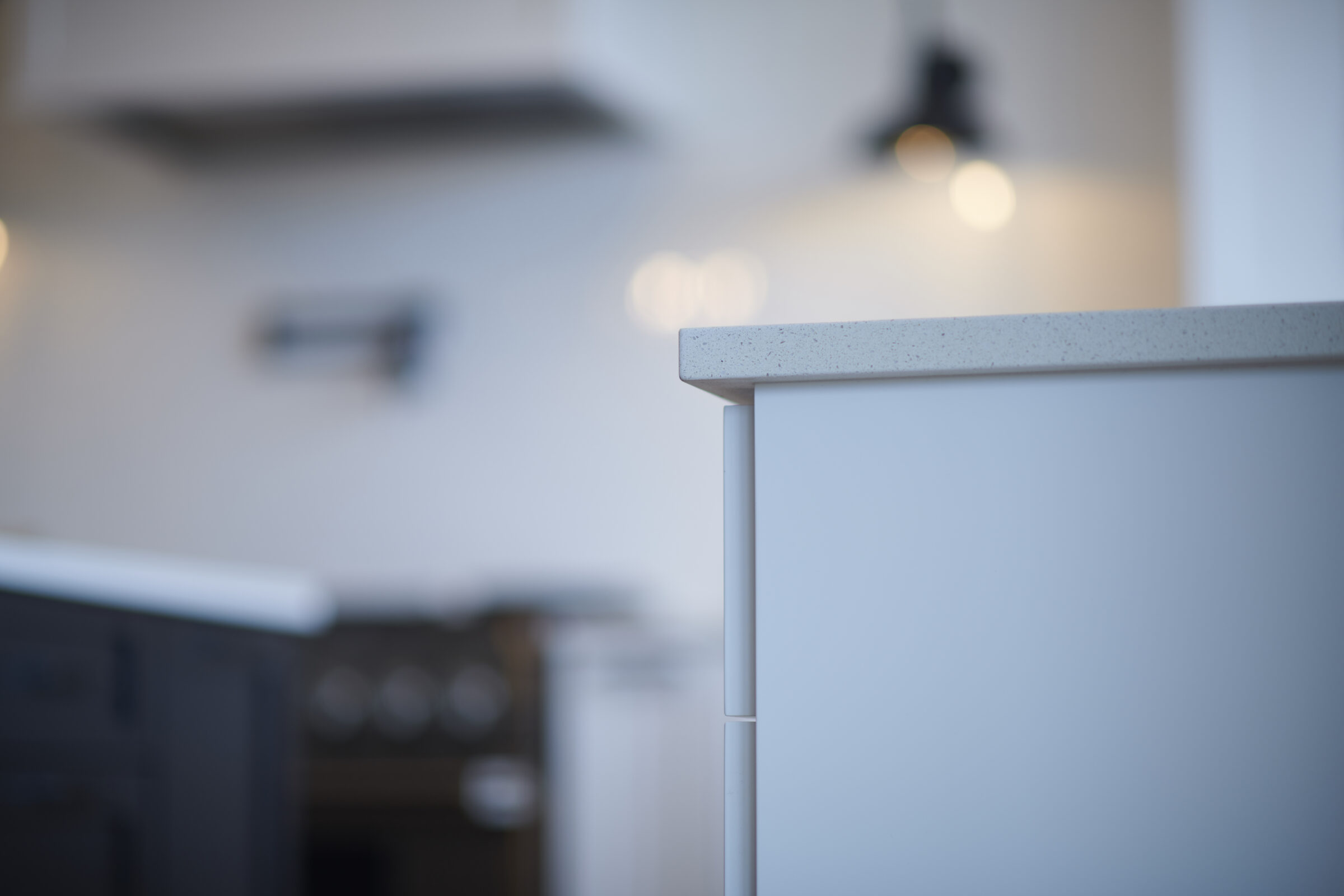 This image depicts a modern kitchen counter corner, with a blurred background showcasing cabinets, a wall-mounted light, and a minimalist design aesthetic.