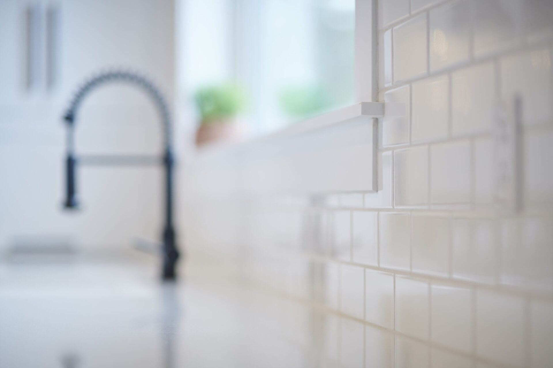 The image shows a modern kitchen with a focus on white subway tiles and a blurred black kitchen faucet in the background, suggesting a clean, sleek design.