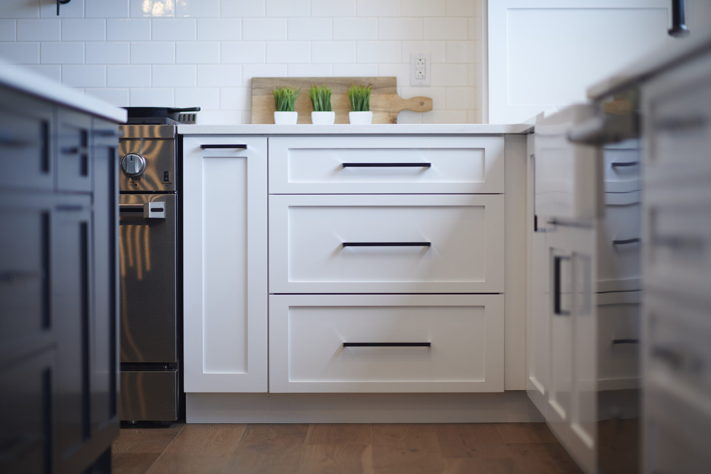 A modern kitchen interior with white cabinets, stainless steel appliances, subway tile backsplash, and wooden countertops with potted plants.