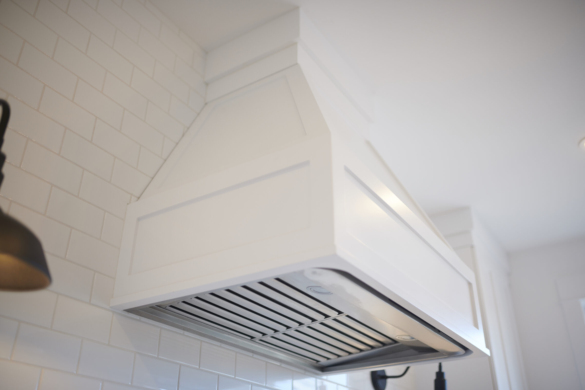 The image shows a modern kitchen range hood against a subway tile backsplash, with a clear focus on clean lines and a bright, white color scheme.