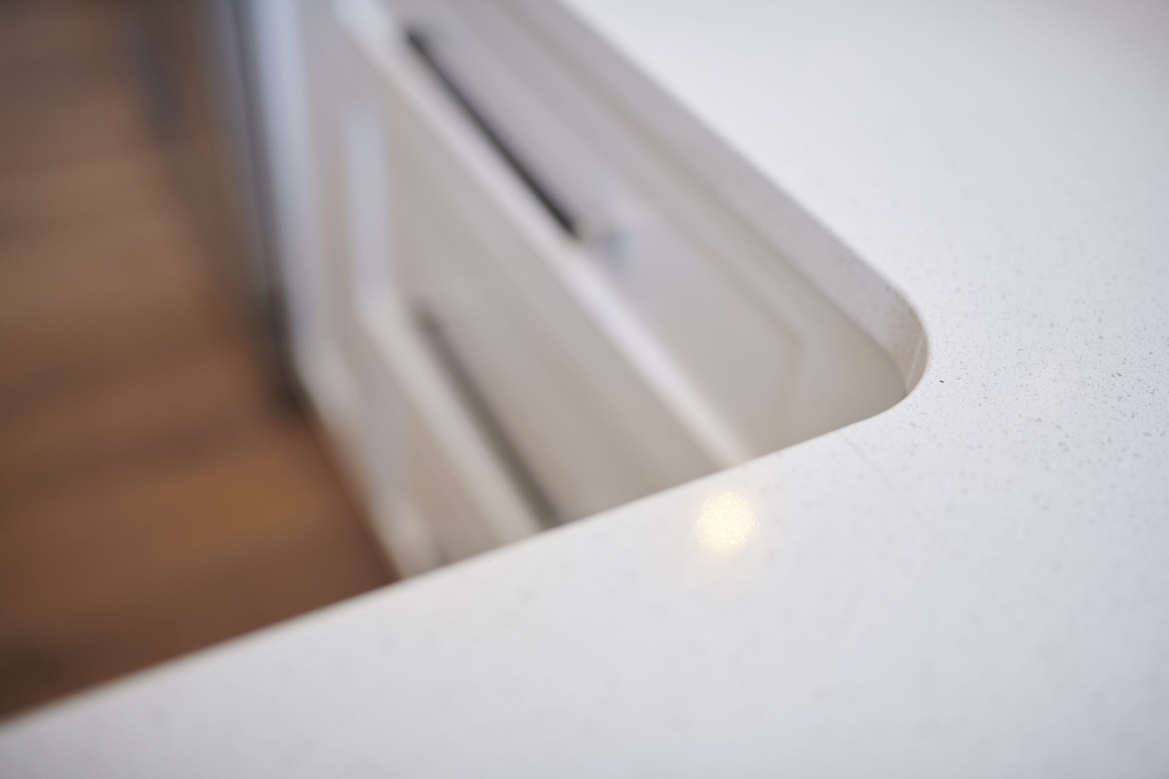 Close-up of a modern, integrated kitchen sink countertop with a blurred background, emphasizing the sleek design and minimalistic style.