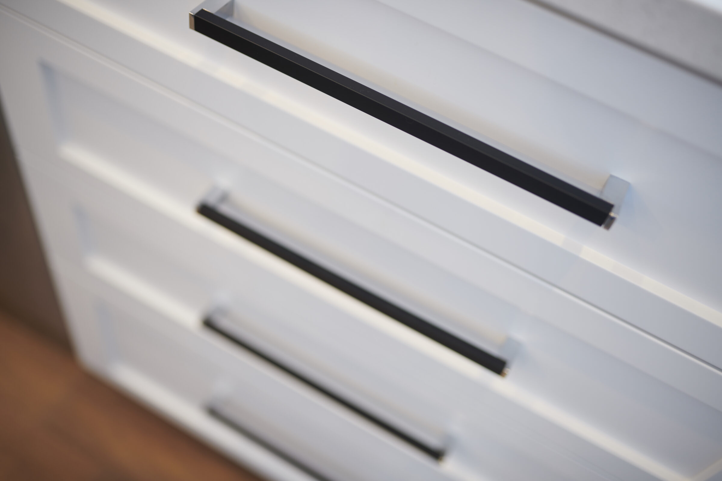 This is a close-up of a contemporary white chest of drawers with sleek black handles. The focus is on the top drawer.