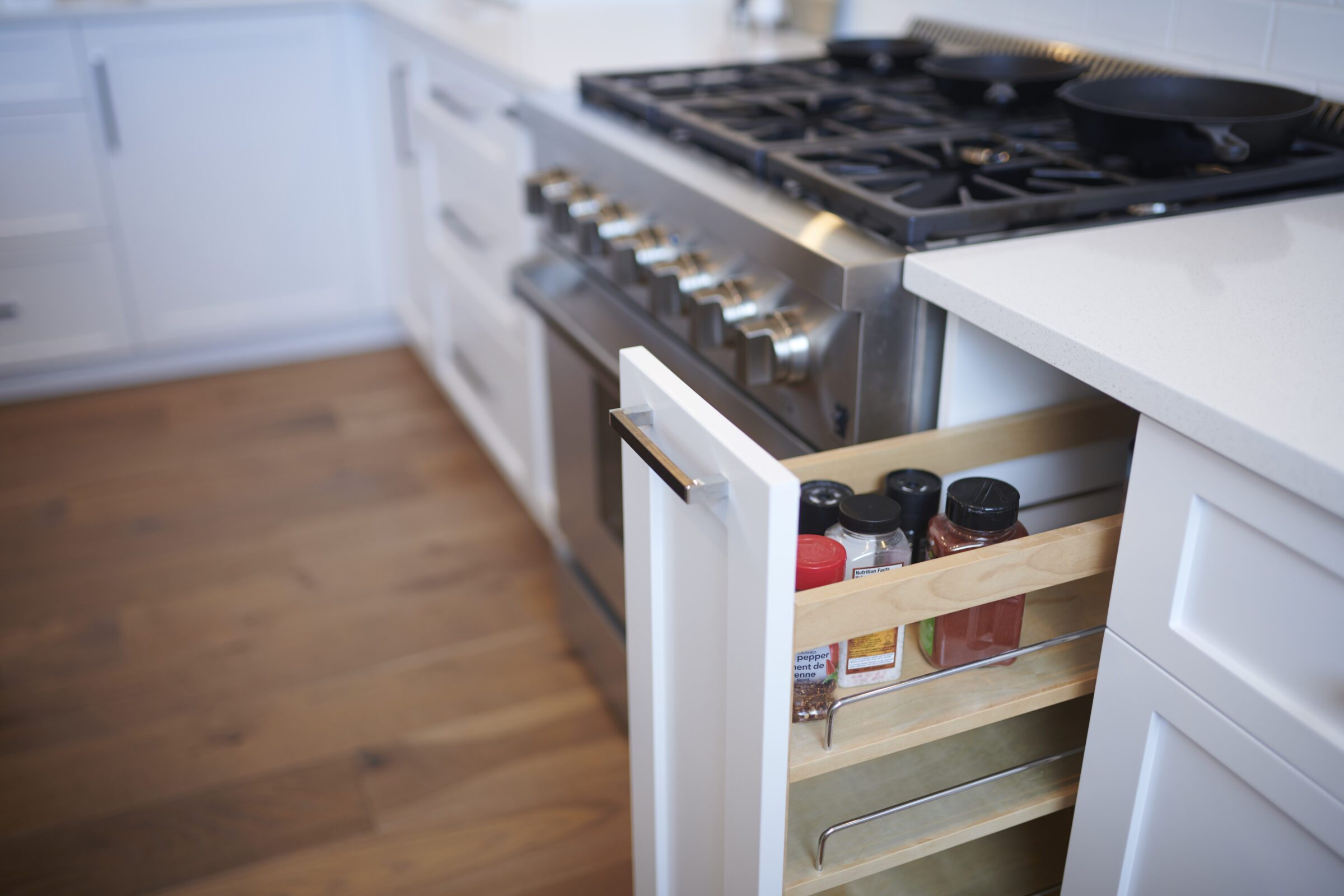 A modern kitchen interior with a gas stove and a pull-out spice rack drawer open, revealing assorted spice jars, in a clean, bright setting.