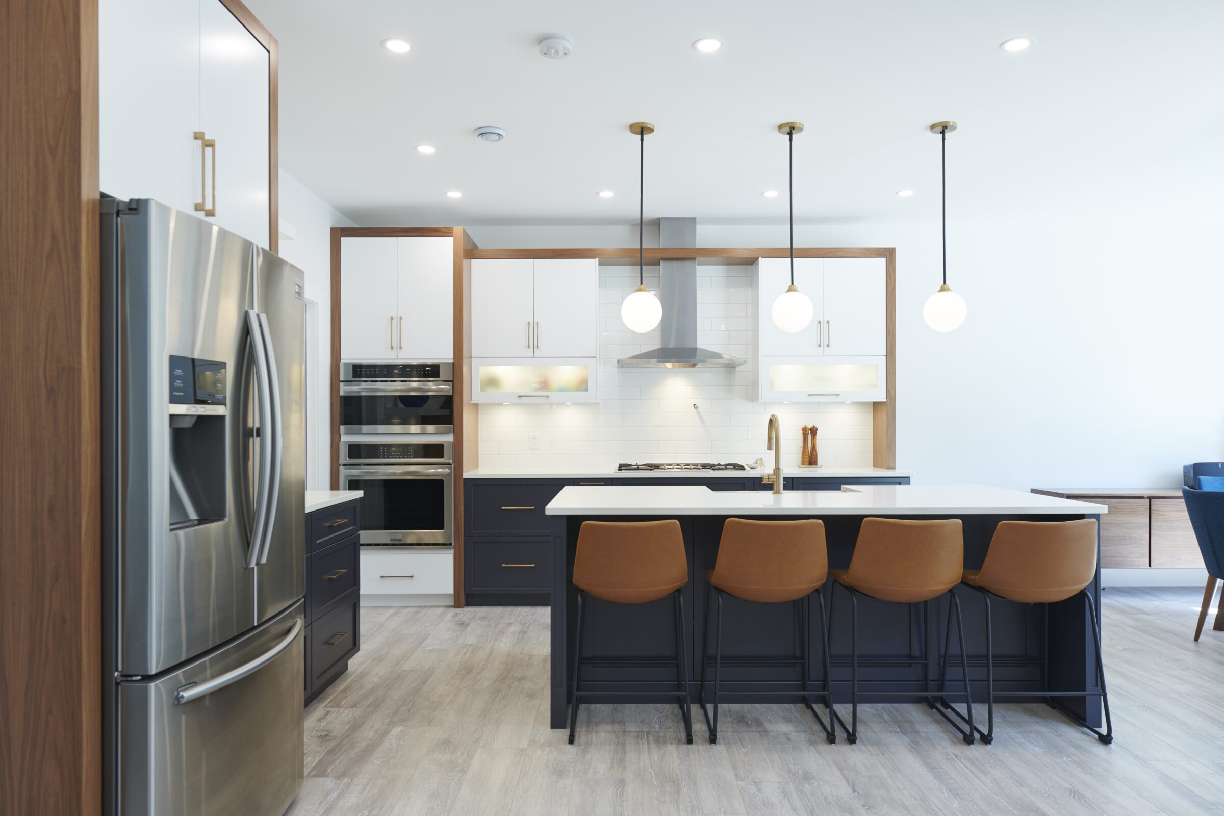 Modern kitchen interior with white walls featuring stainless steel appliances, dark cabinetry, pendant lights, and a central island with bar stools.