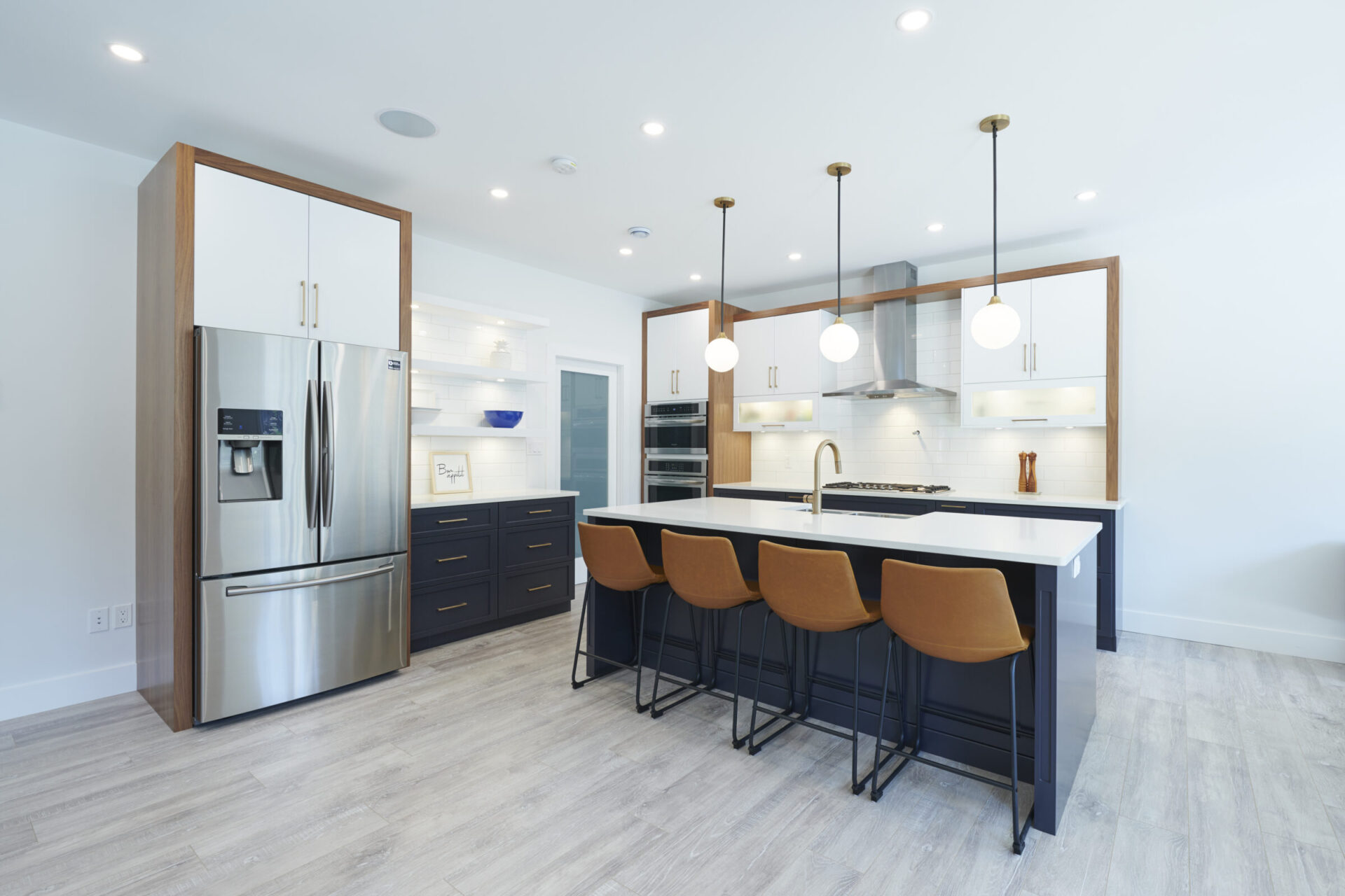 Modern kitchen interior with stainless steel appliances, dark blue cabinets, white countertops, pendant lights, and brown bar stools at the island.