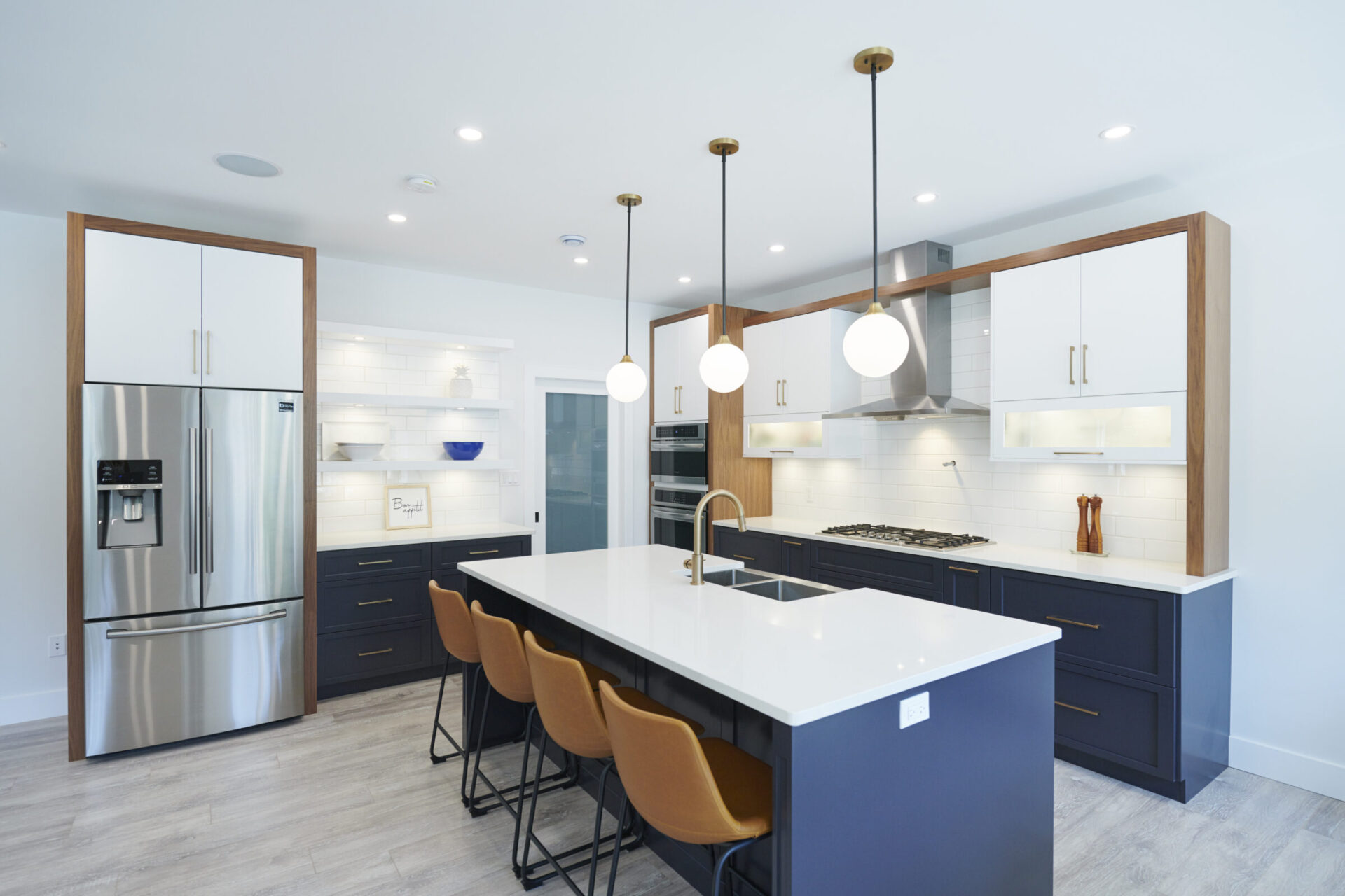 This image shows a modern kitchen interior with white countertops, blue cabinets, stainless steel appliances, pendant lighting, and a central island with stools.