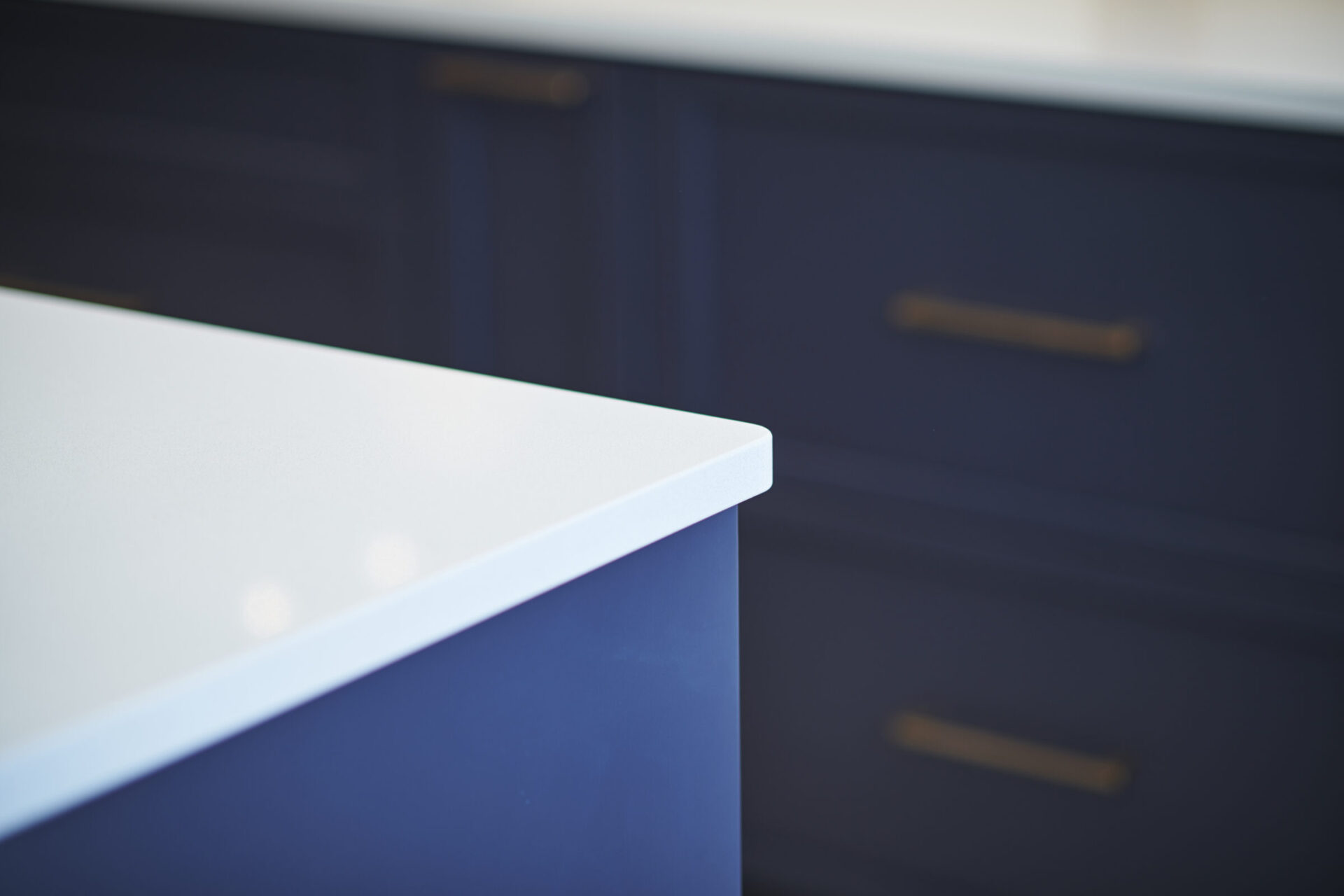 A close-up of a kitchen with a white countertop. Navy blue cabinets with gold handles are visible in the background, slightly out of focus.