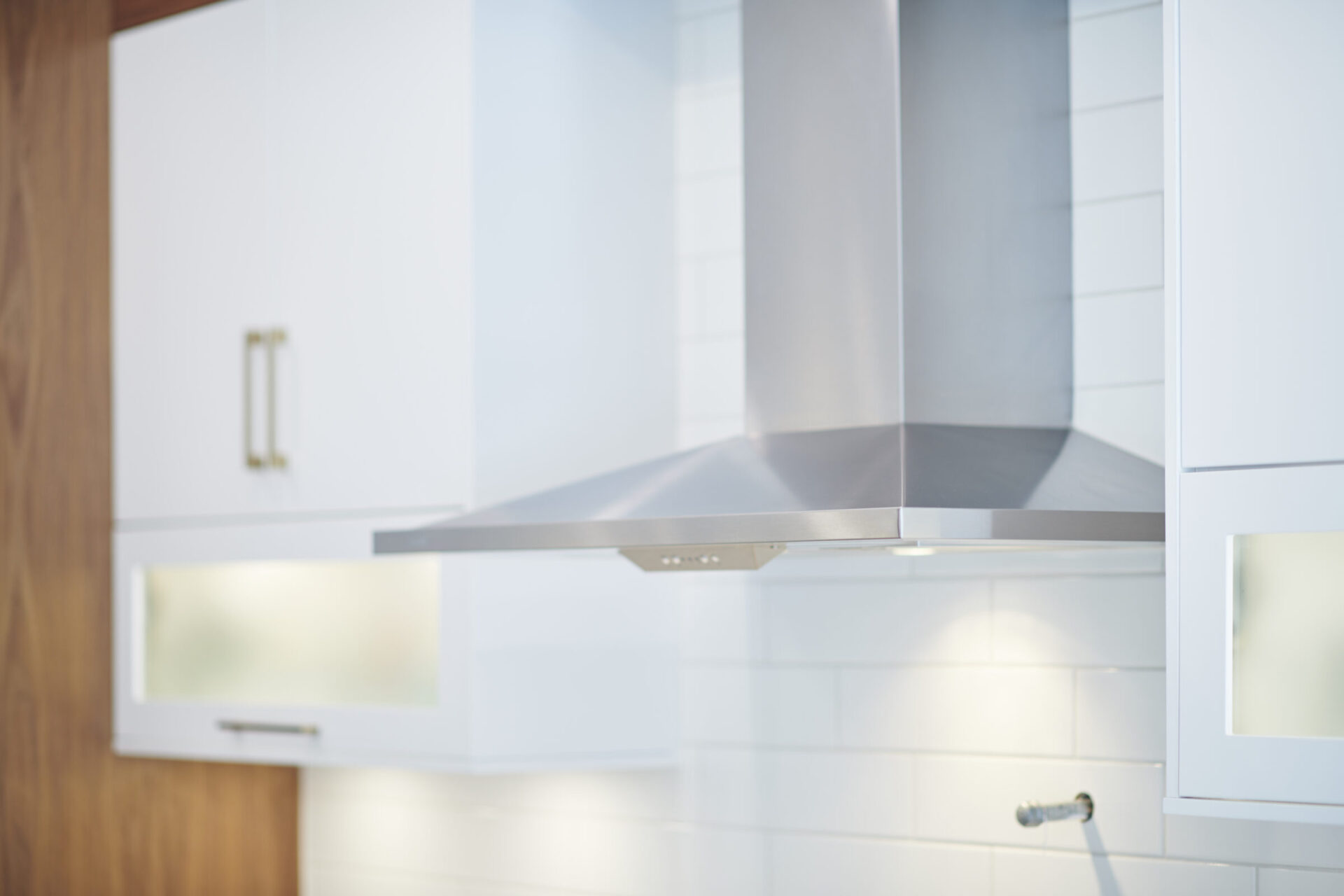 This image shows a modern kitchen with a stainless steel range hood, white cabinets, and a subtle wooden accent. The focus is on clean lines and simplicity.