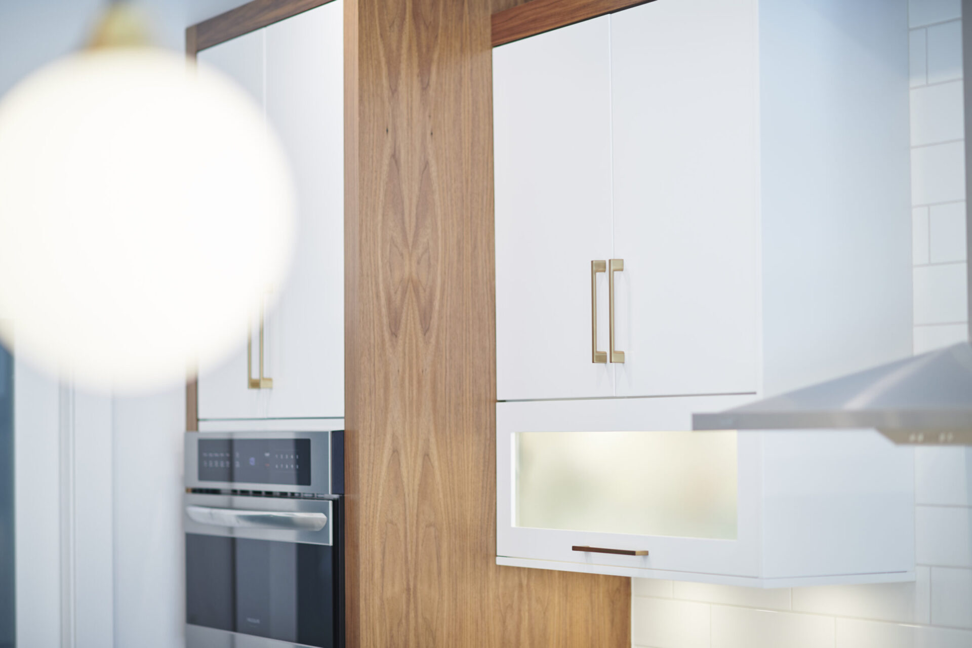 Modern kitchen interior with white cabinets, a wooden pillar, and stainless steel appliances framed by soft-focus lighting in the foreground.